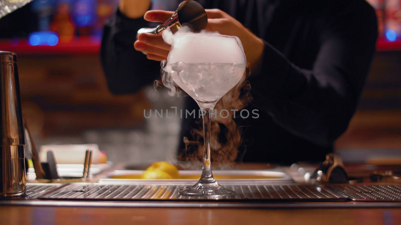 Barman cooking drink with dry ice. Wine glass wrapped in steam on the bar counter. Bartender pouring an alcoholic drink into it
