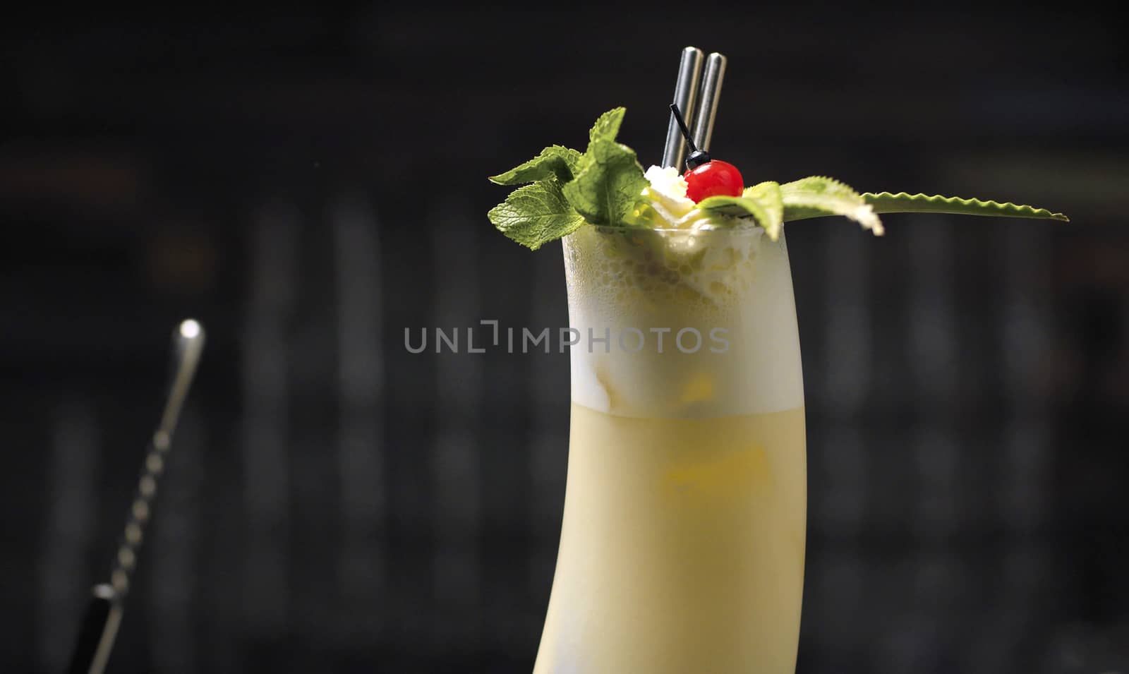 Close up glass of pina colada coctail garnished with whipped cream, mint, cherry and pineapple leaves.