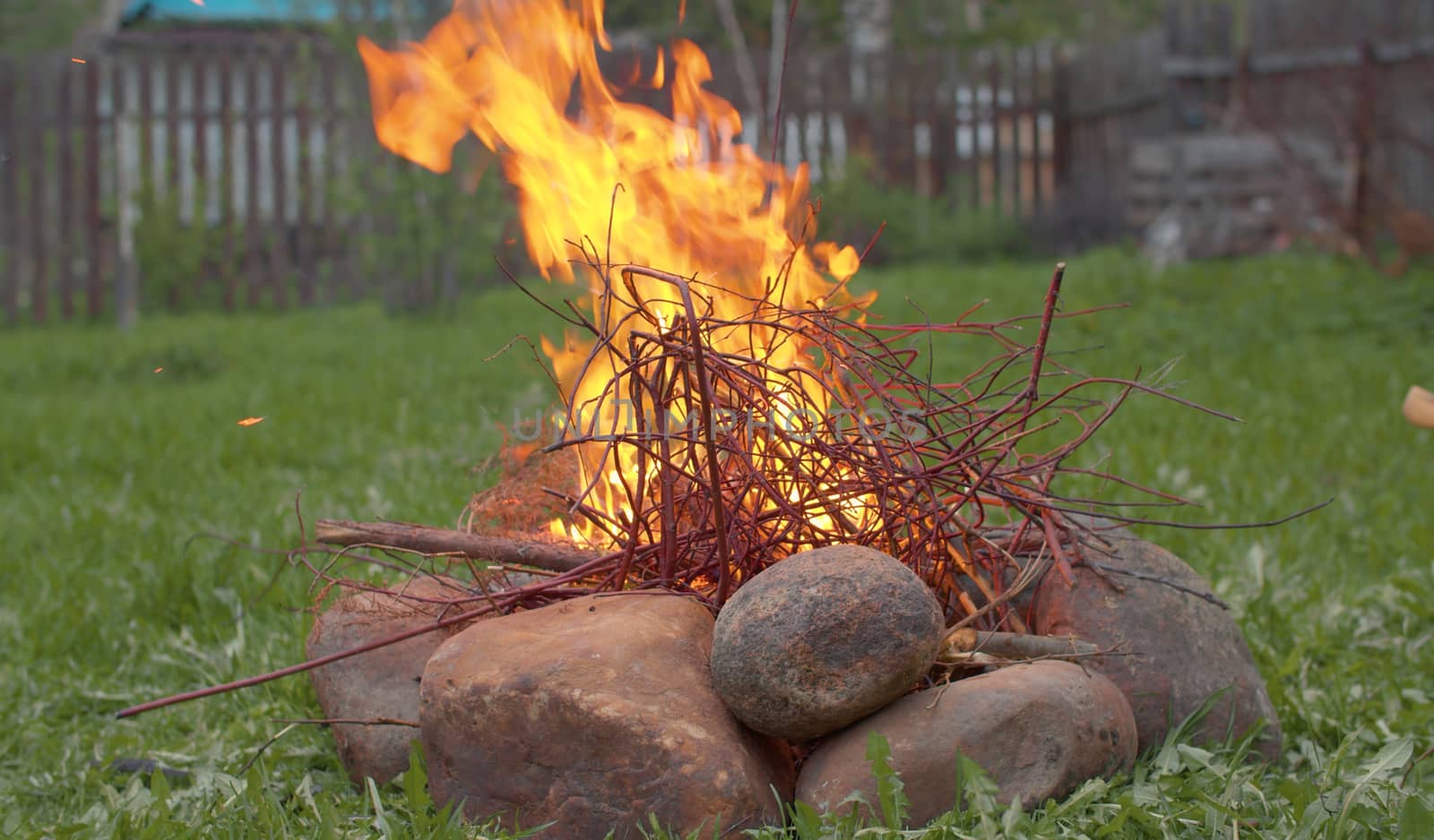 Bonfire burning in the yard of a country house. Thin tree branches and brushwood burn among stones in a meadow on a spring day.