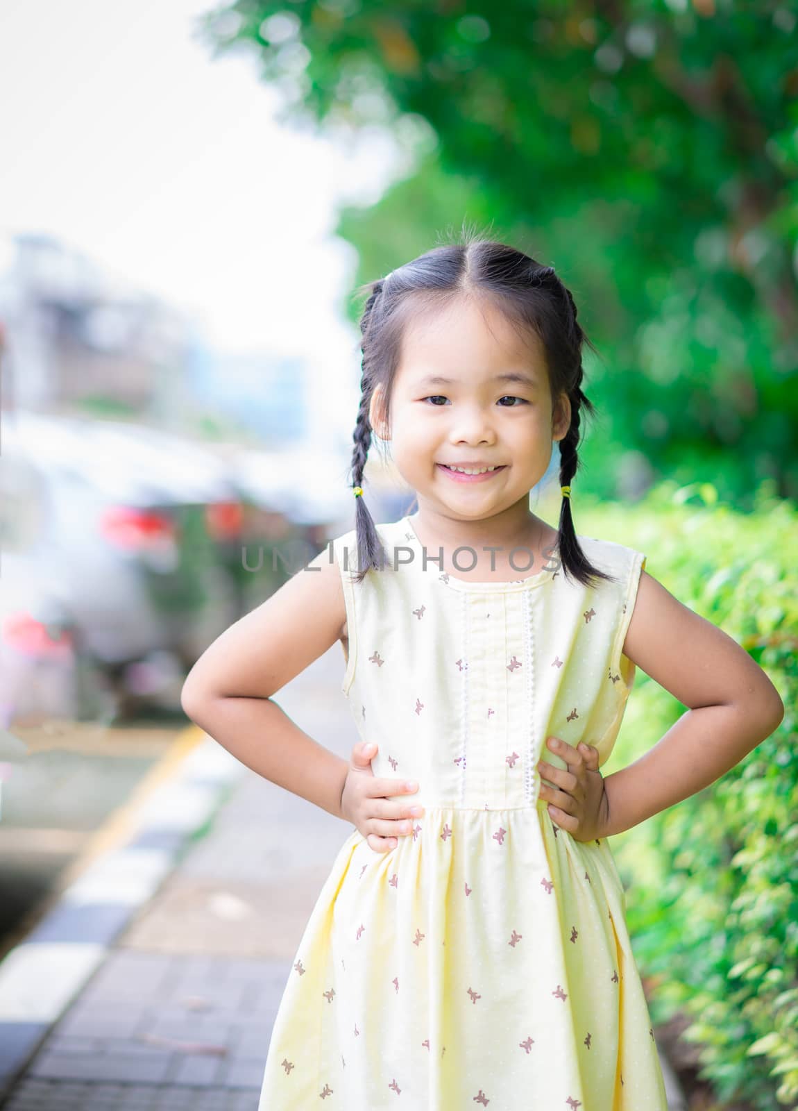 Portrait of happy asian little girl in dress standing on footpath in the park