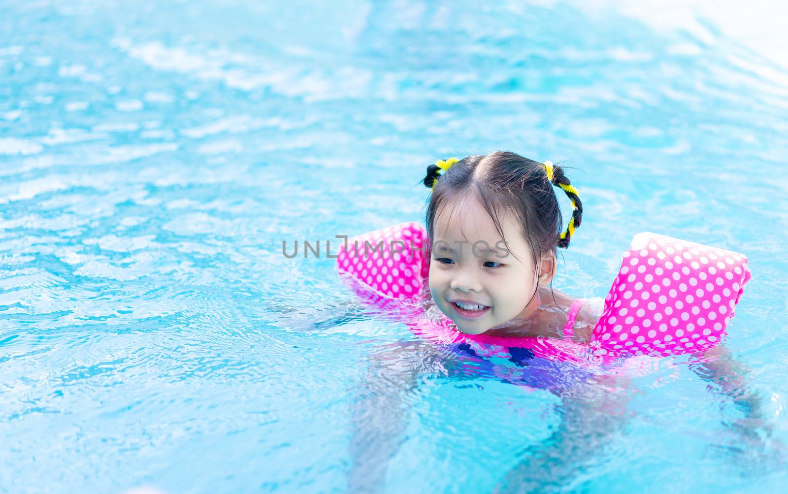 little asian girl wearing inflatable sleeves swimming in the pool