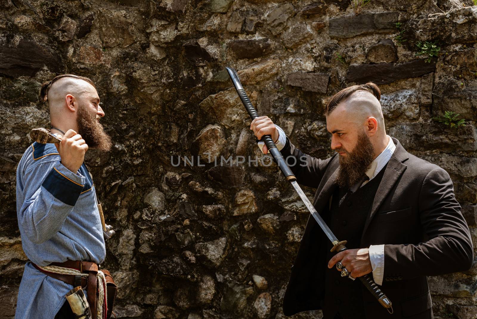 A man in Viking clothes derides his alter ego which challenges him by brandishing a katana in contemporary clothes, the same man face to face in clothes from different eras