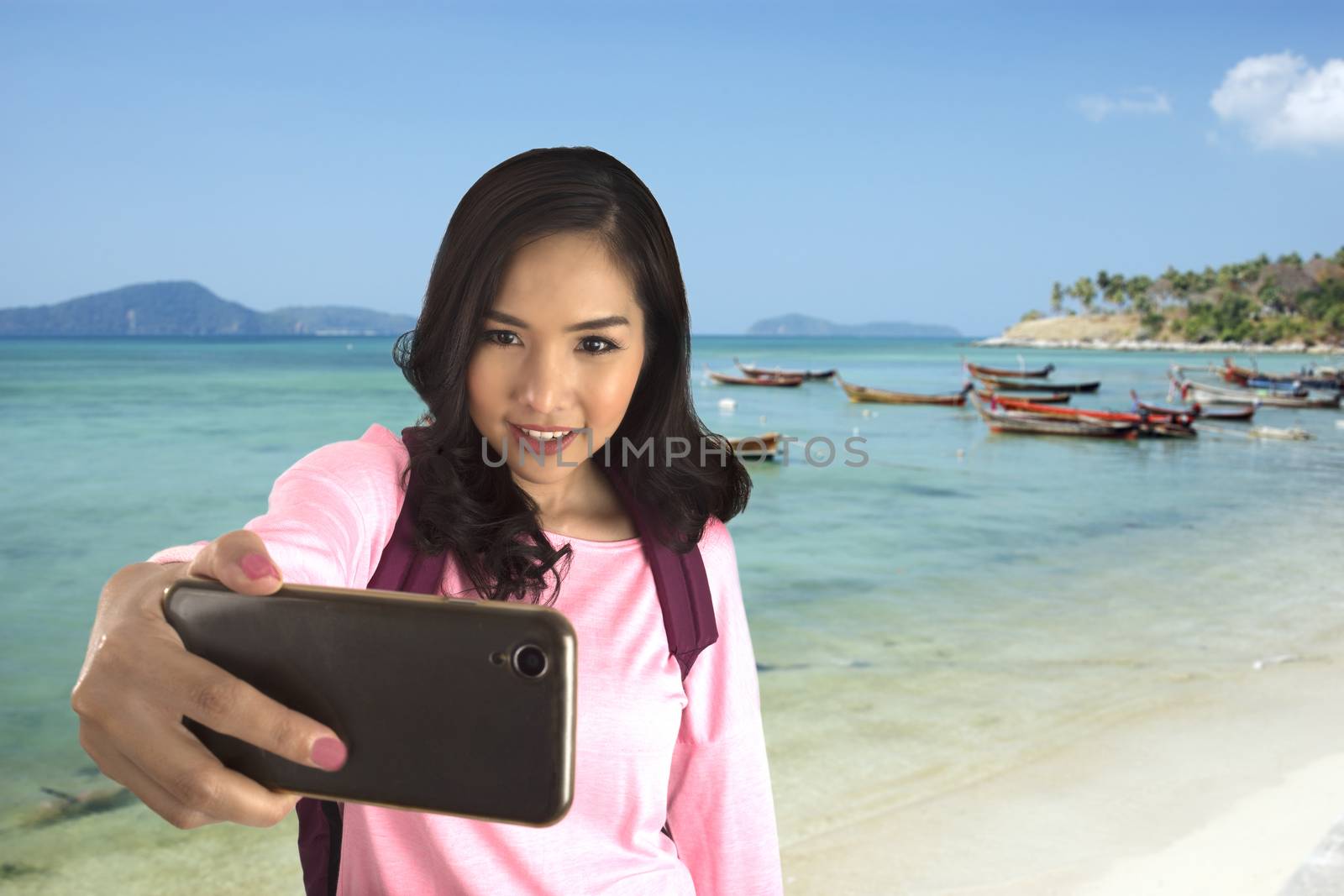 Tourist girl take selfie photo with beautiful sea in background by smartphone in her hand.