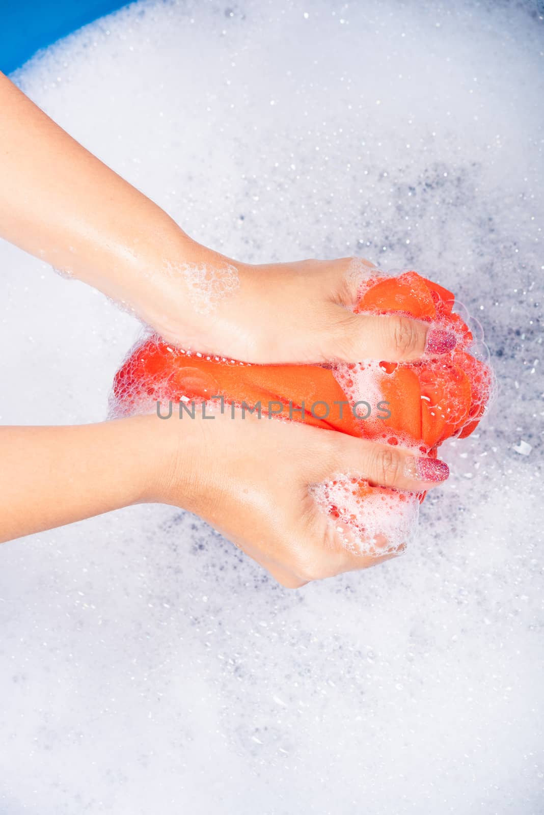 Closeup young Asian woman use hands washing color clothes in basin with detergent have soapy bubble water, studio shot background, laundry concept