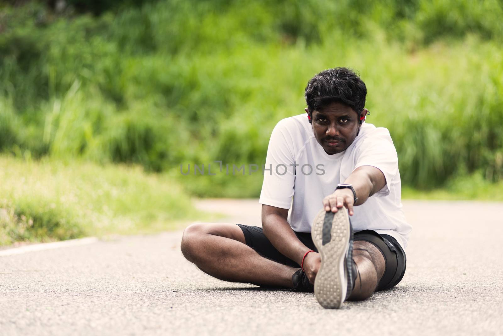 Close up Asian young athlete sport runner black man wear watch he sitting pull toe feet stretching legs and knee before running at outdoor street health park, healthy exercise before workout concept