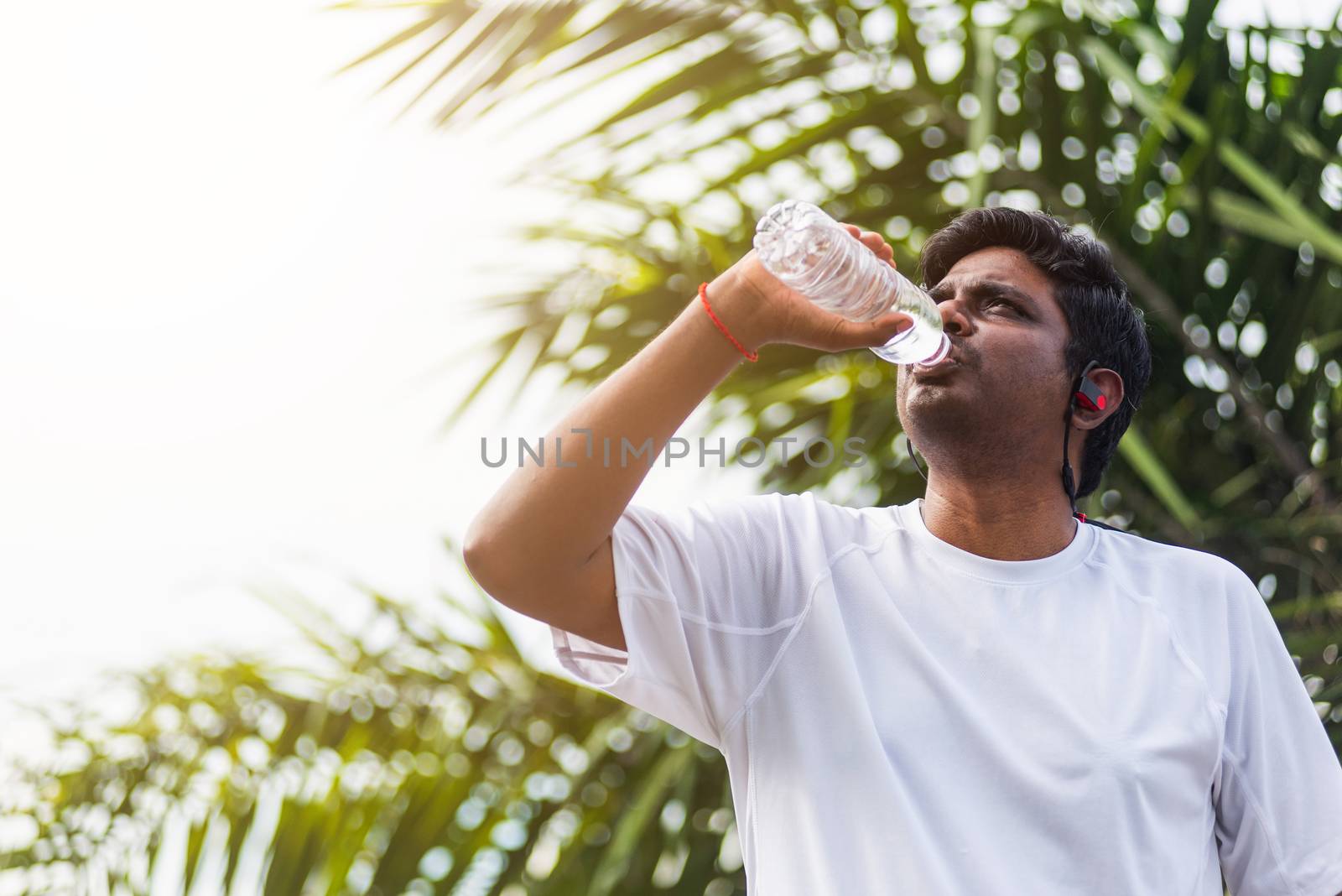 Close up Asian young sport runner black man wear athlete headphones he drinking water from a bottle after running at the outdoor street health park, healthy exercise workout concept