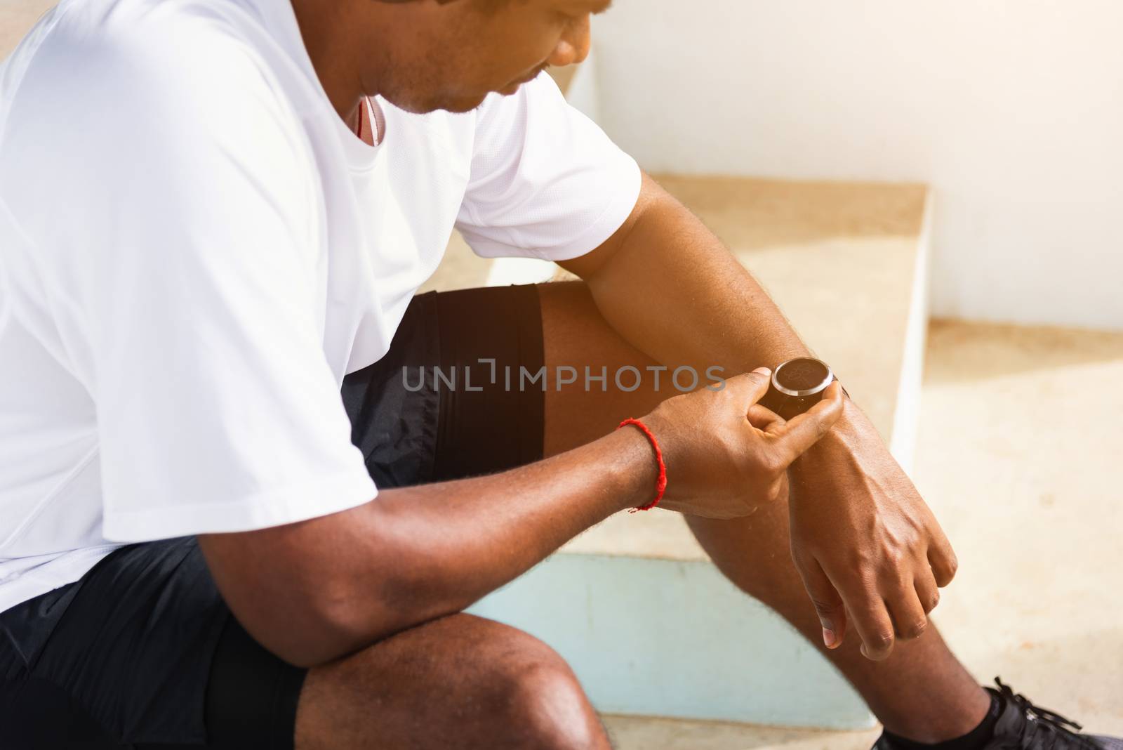 Close up Asian young athlete sport runner black man wear modern time smart watch he sitting resting before training running at the outdoor street health park, healthy exercise before workout concept