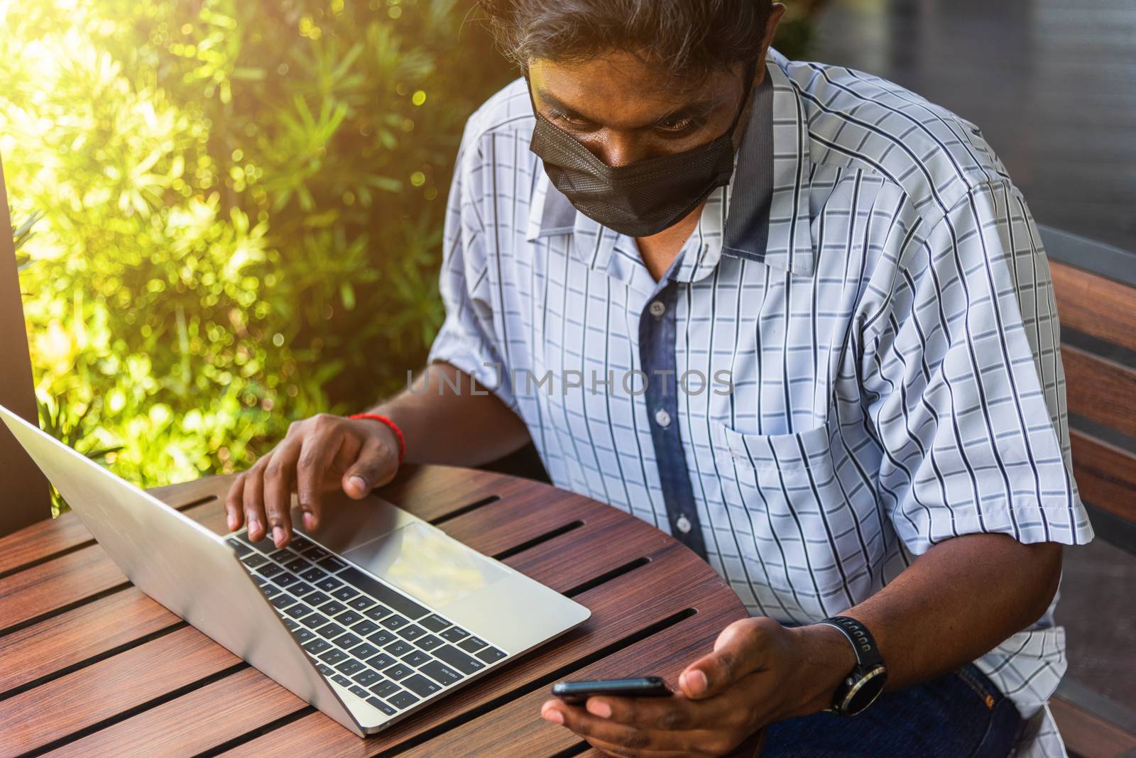 Happy Asian hand black man person working with laptop computer and reading message from modern smart phone blank screen device technology and connecting networking online at the coffee cafe shop