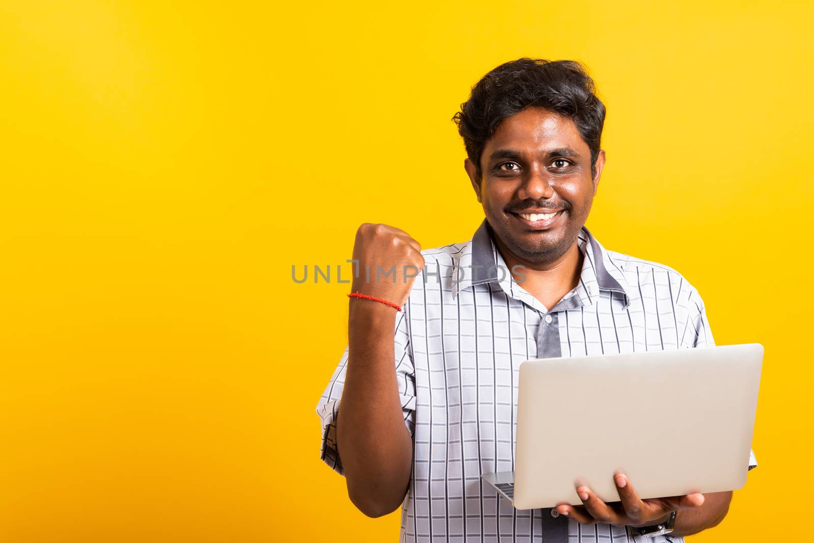 Closeup Asian happy portrait young black man excited holding laptop computer clenching fists and raising a hand for winner sign celebrating his success, studio shot isolated on yellow background
