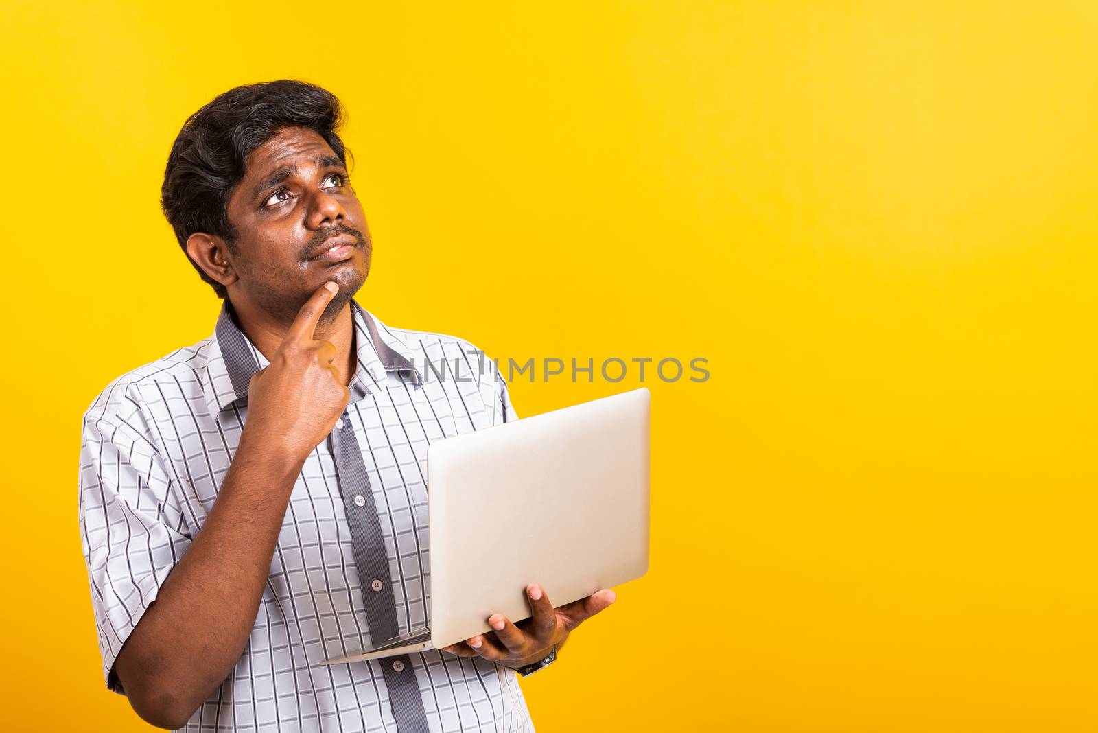Closeup Asian happy portrait young black man holds a laptop computer hand finger handle on the chin and thinking question looking away, studio isolated on yellow background
