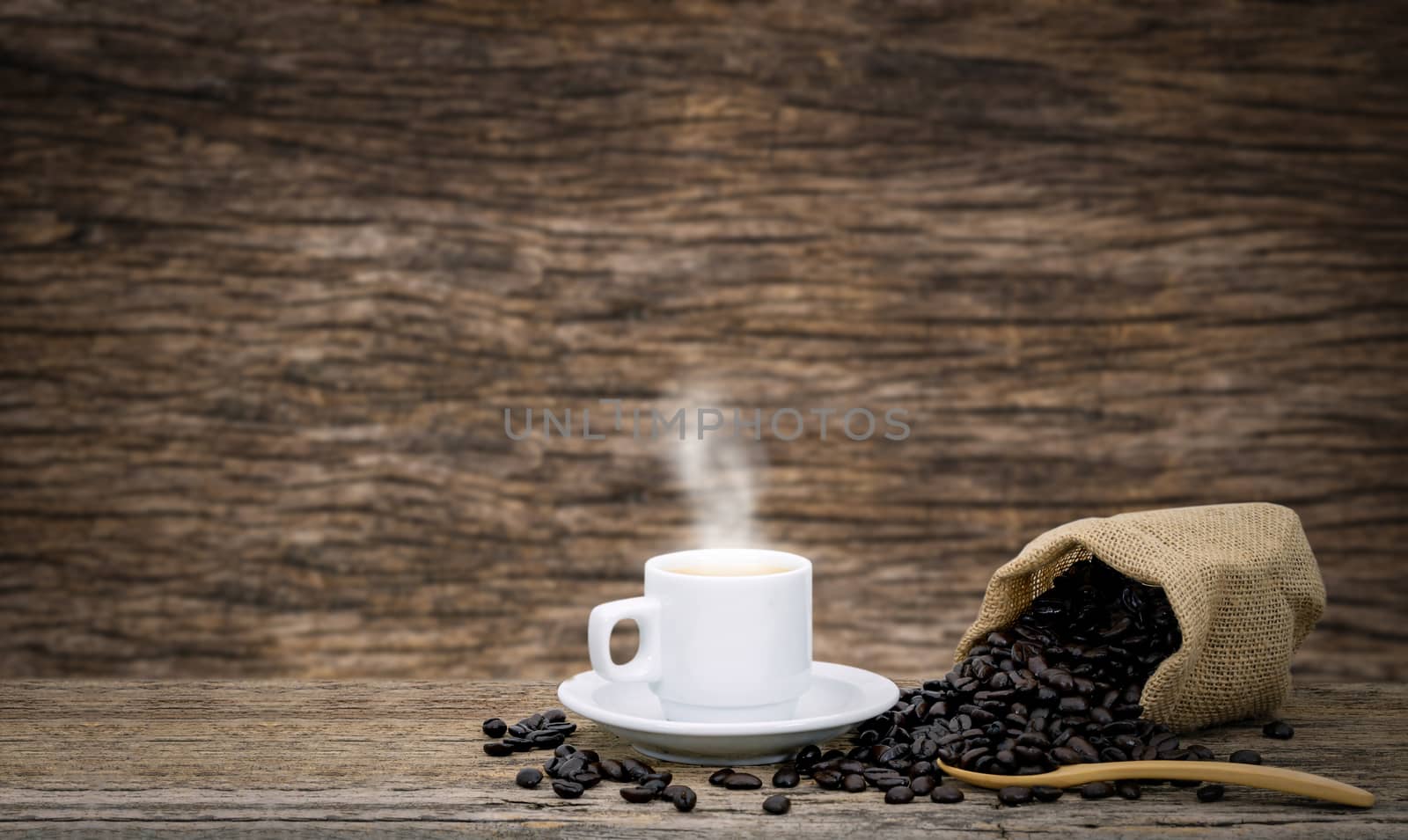 Coffee cup and coffee beans roasted in a sack on a wooden floor.