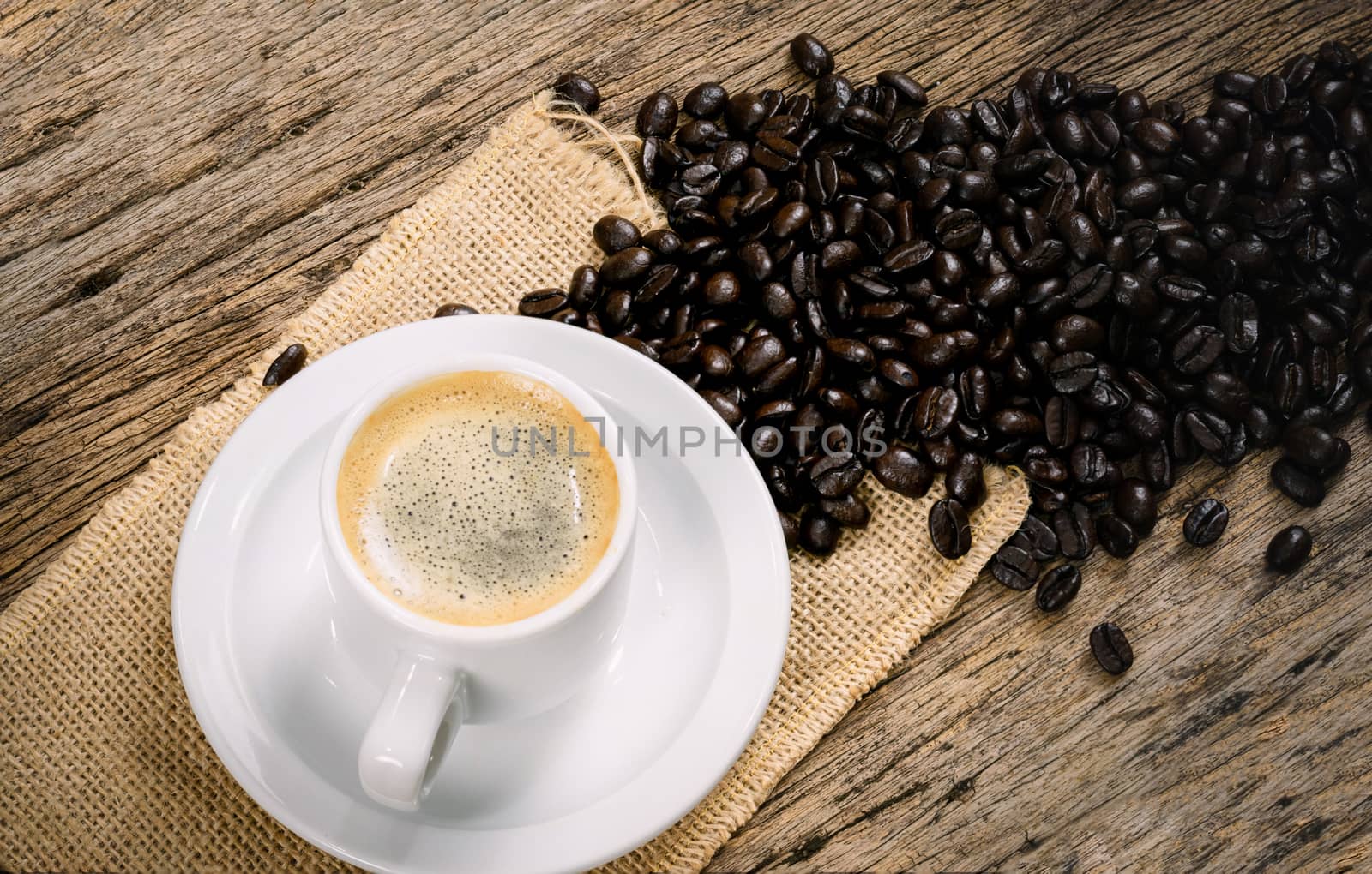 Coffee cup and coffee beans roasted in a sack on a wooden floor.