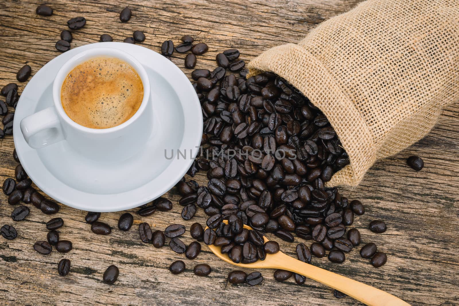Coffee cup and coffee beans roasted in a sack on a wooden floor.