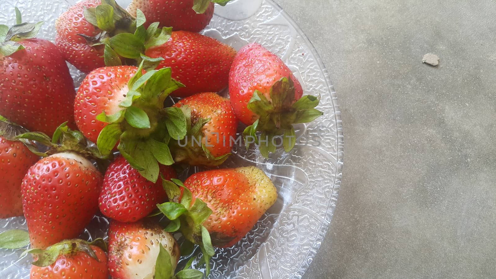 Top view with selective focus of sweet fresh strawberries with green leaves in plate on grey floor background.