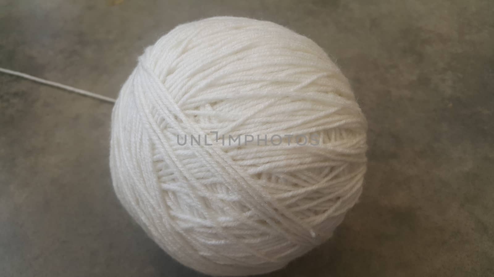 Off white ball of threads wool yarn for knitting on grey floor background by Photochowk