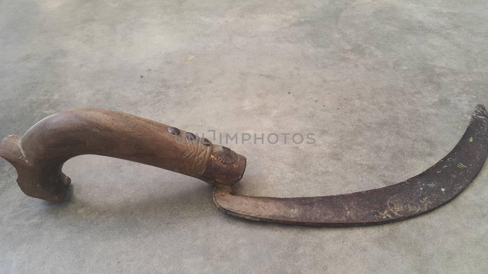 Close-up view of an old sickle (bagging hook or reaping-hook) on the concrete surface. Traditional hand-held agricultural tool.