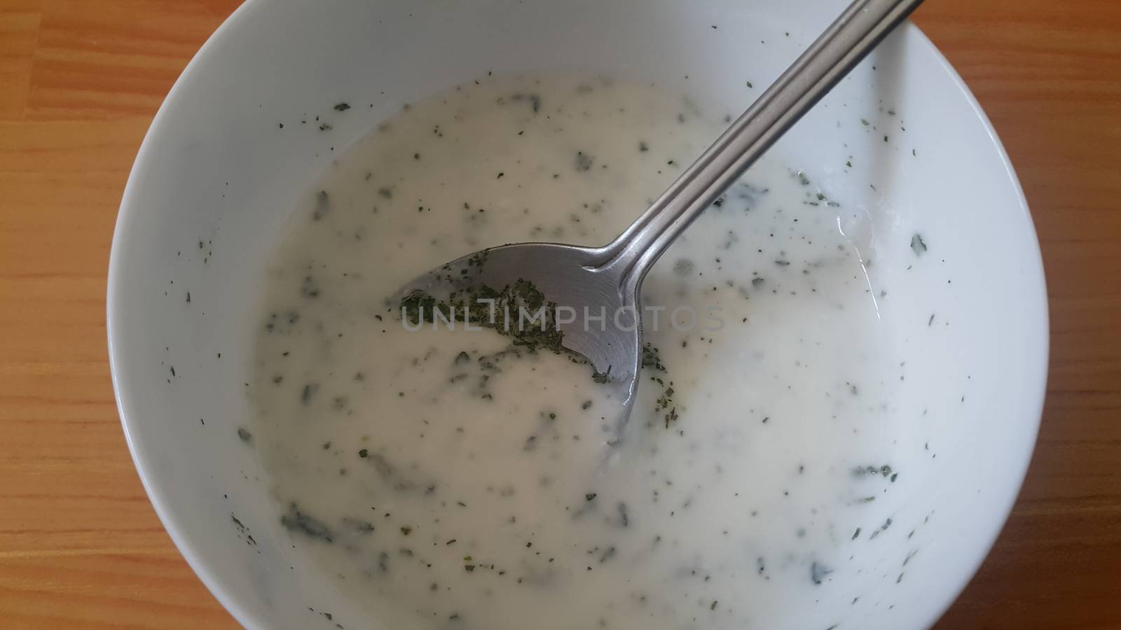 Close up of plain curd or yogurt or dahi in white ceramic bowl with silver spoon by Photochowk