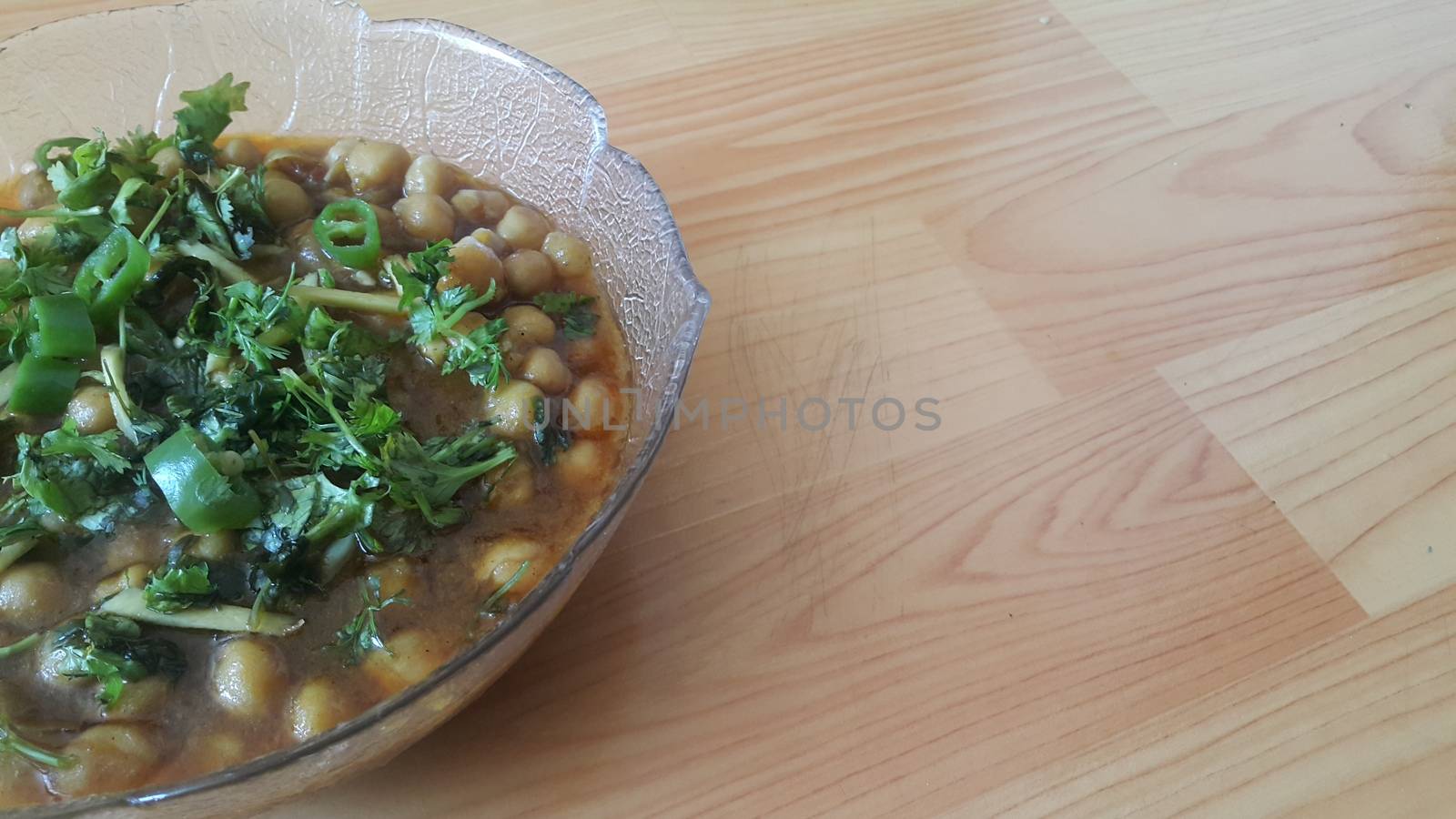 Home made dish served in glass bowl garnished with sliced onion and green coriander leaf and placed over wooden floor .Traditional lentils Channa Masala or chickpeas curry or chole bhature.