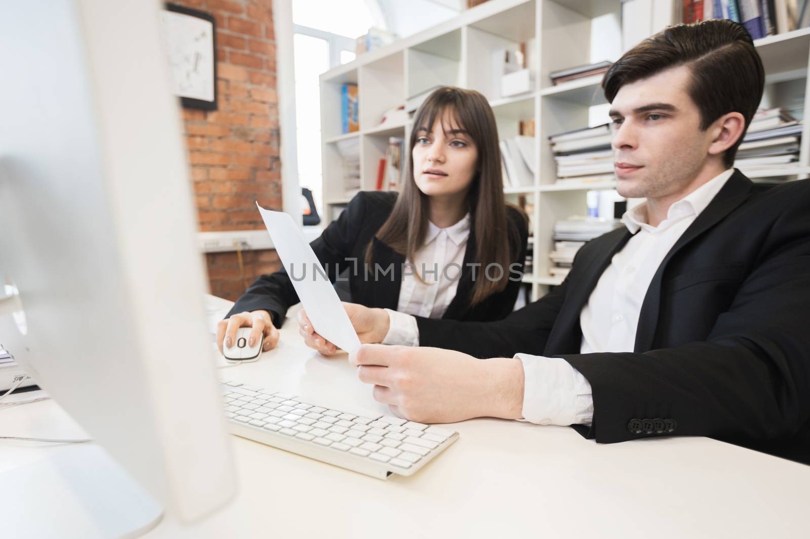 Two business people working together with documents sitting in front of computer monitor in office