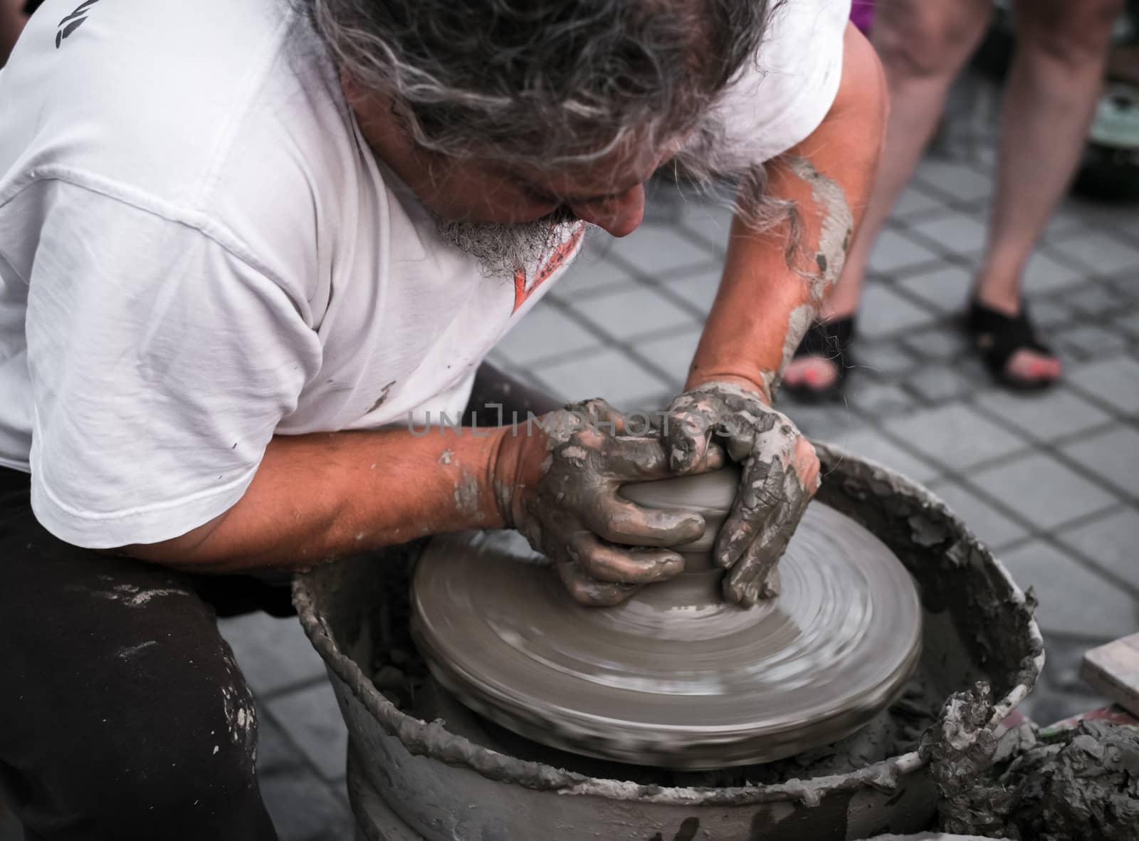 Hands of a potter shaping a clay pot on a potter wheel by Roberto