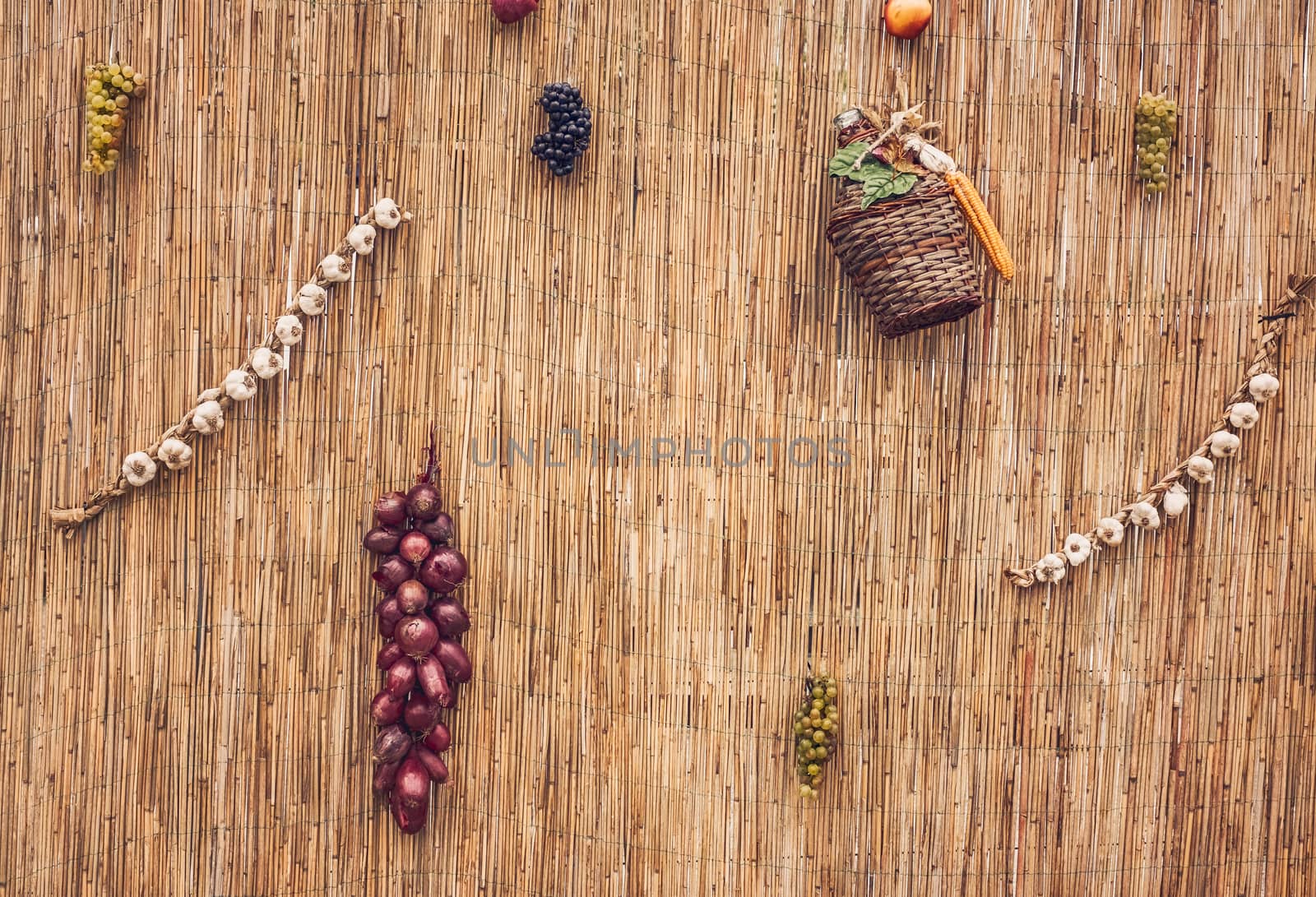 grapes, red onion, corn, garlic and a damigean on a wicker wall