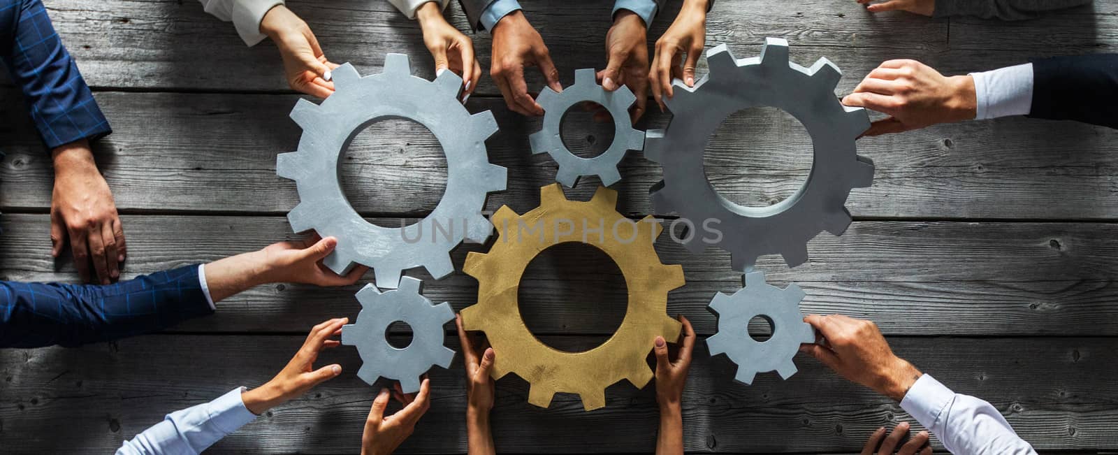 Group of business people joining together silver and golden colored gears on table at workplace top view