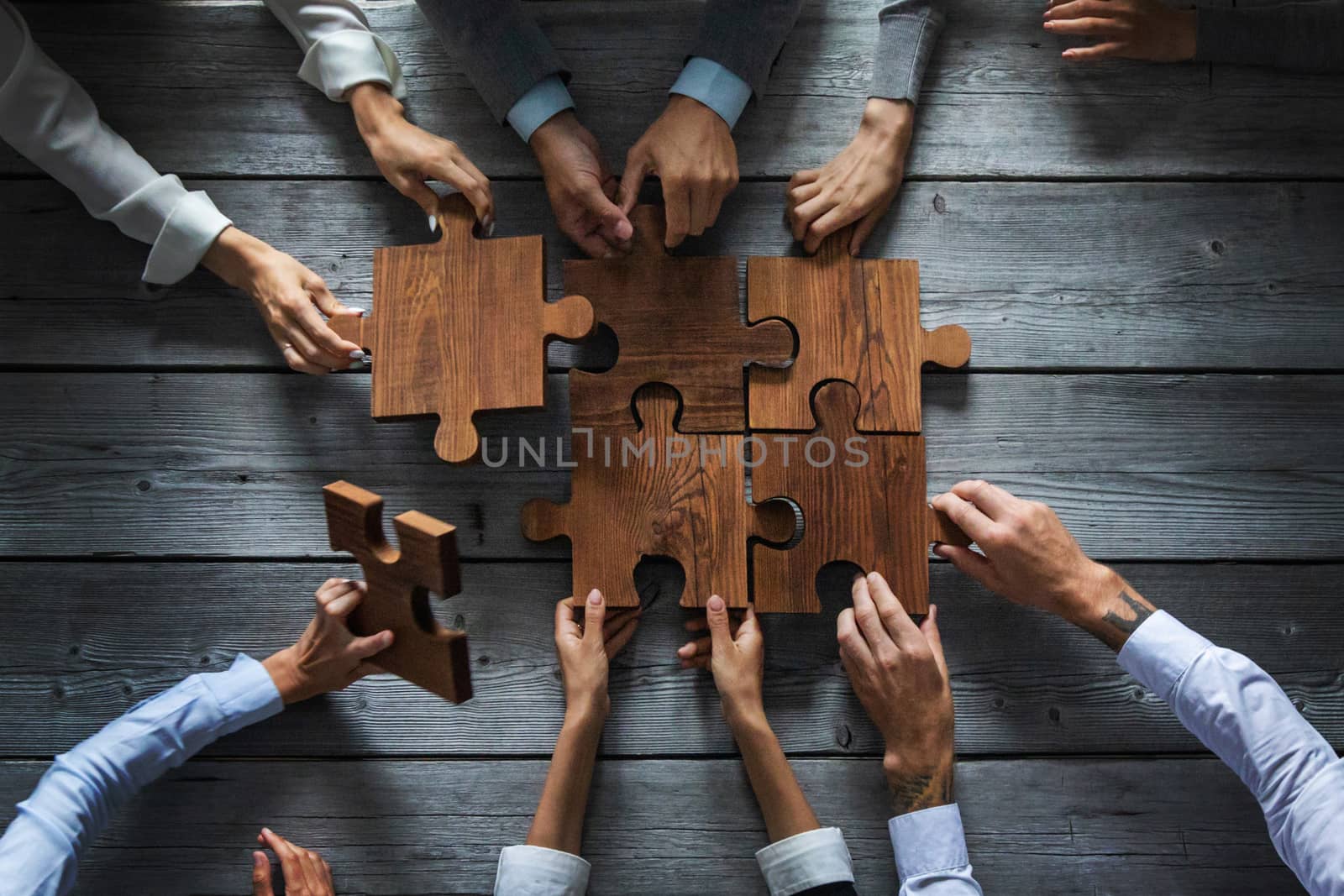 Business people team sitting around meeting table and assembling wooden jigsaw puzzle pieces unity cooperation ideas concept