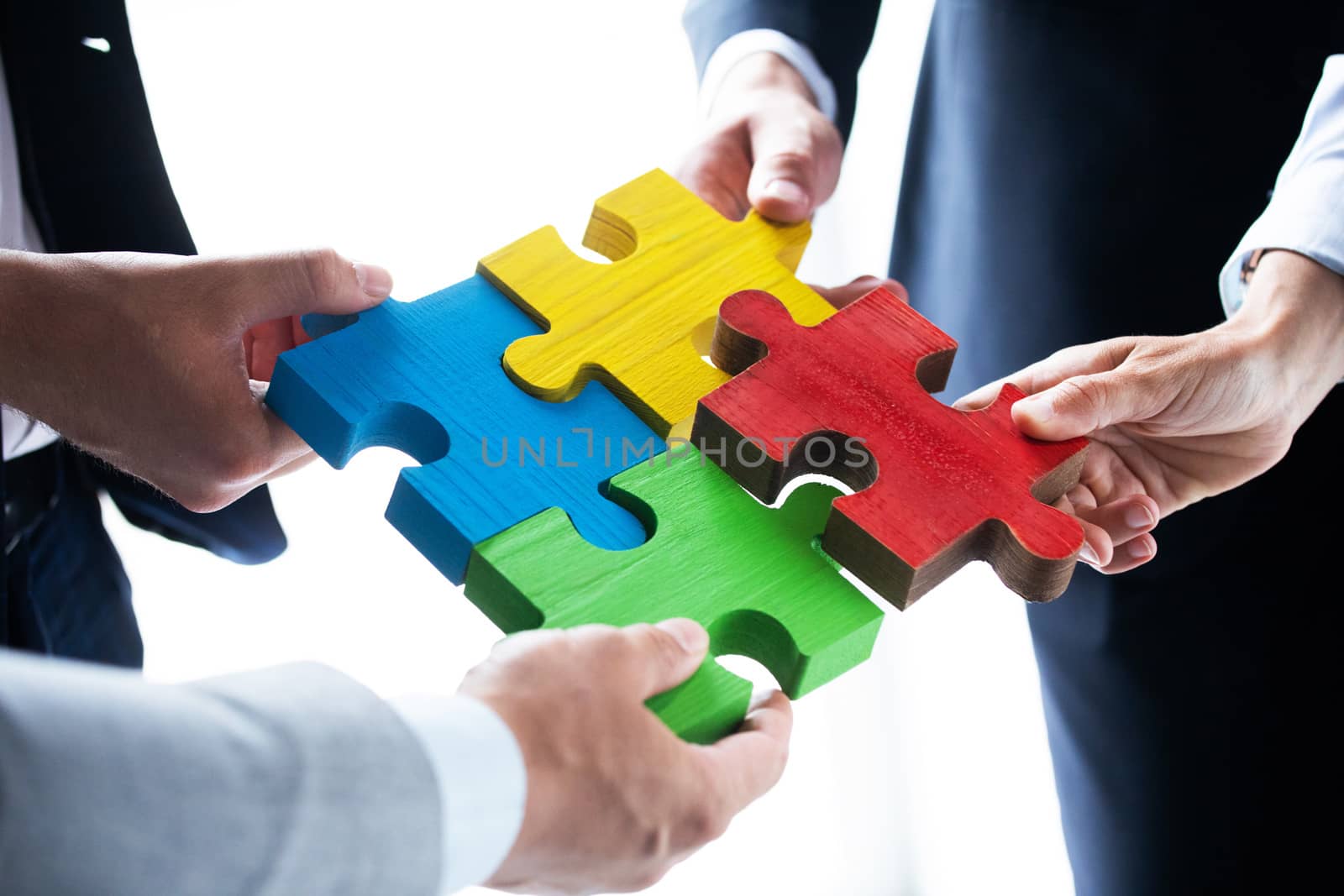 Business people team assembling four color jigsaw puzzle pieces unity cooperation ideas concept