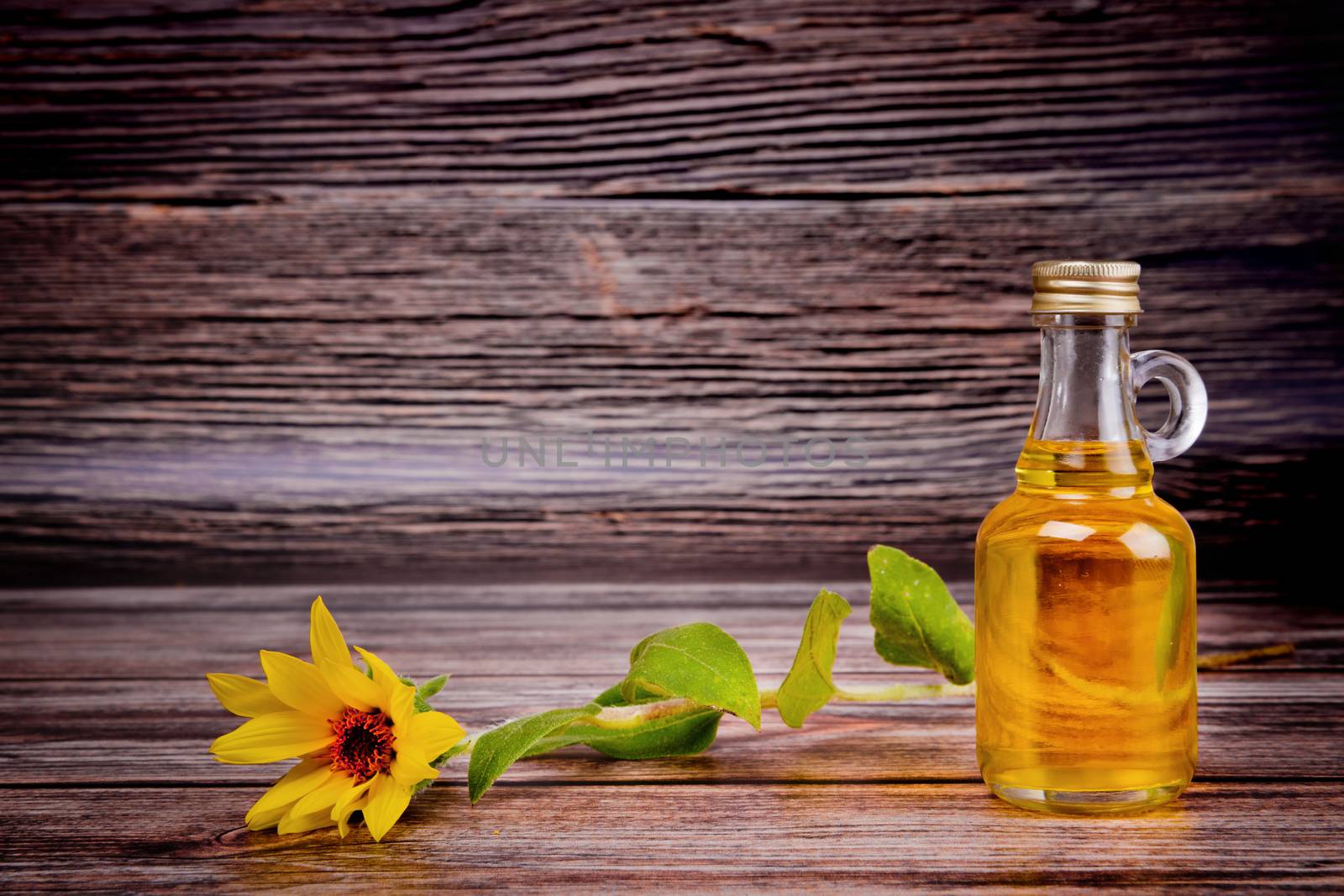 Glass bottle with sunflower oil and sunflower flower on wooden background. Studio shot. by leonik
