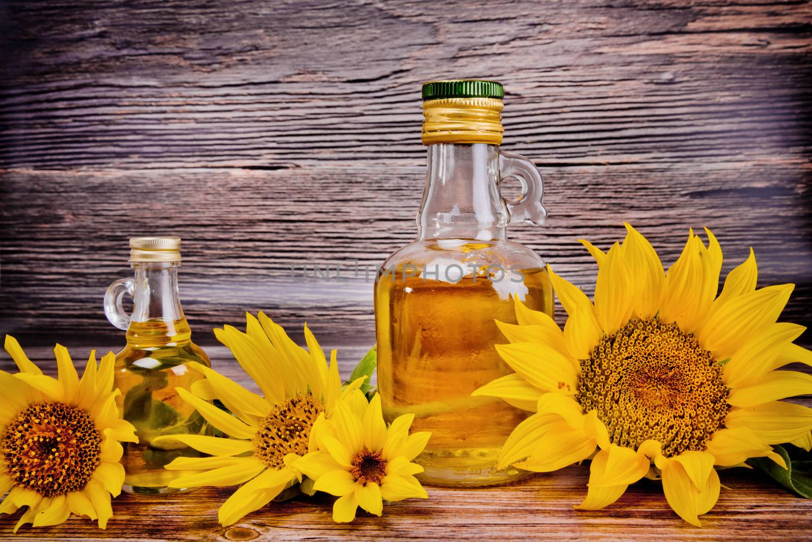 Two glass bottles with sunflower oil and flowers on wooden background. Studio shot. by leonik