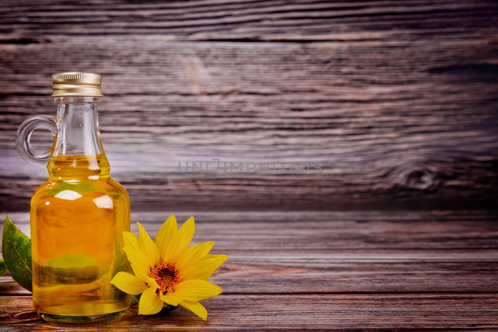 Glass bottle with sunflower oil and flowers on wooden background. Studio shot.