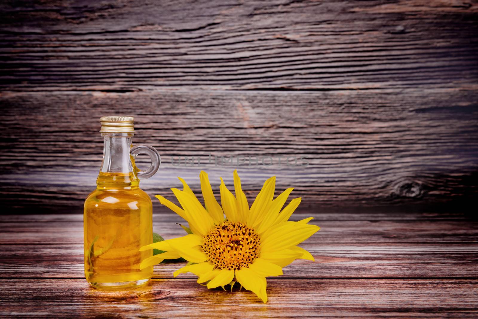 Glass bottle with sunflower oil and flowers on wooden background. Studio shot. by leonik