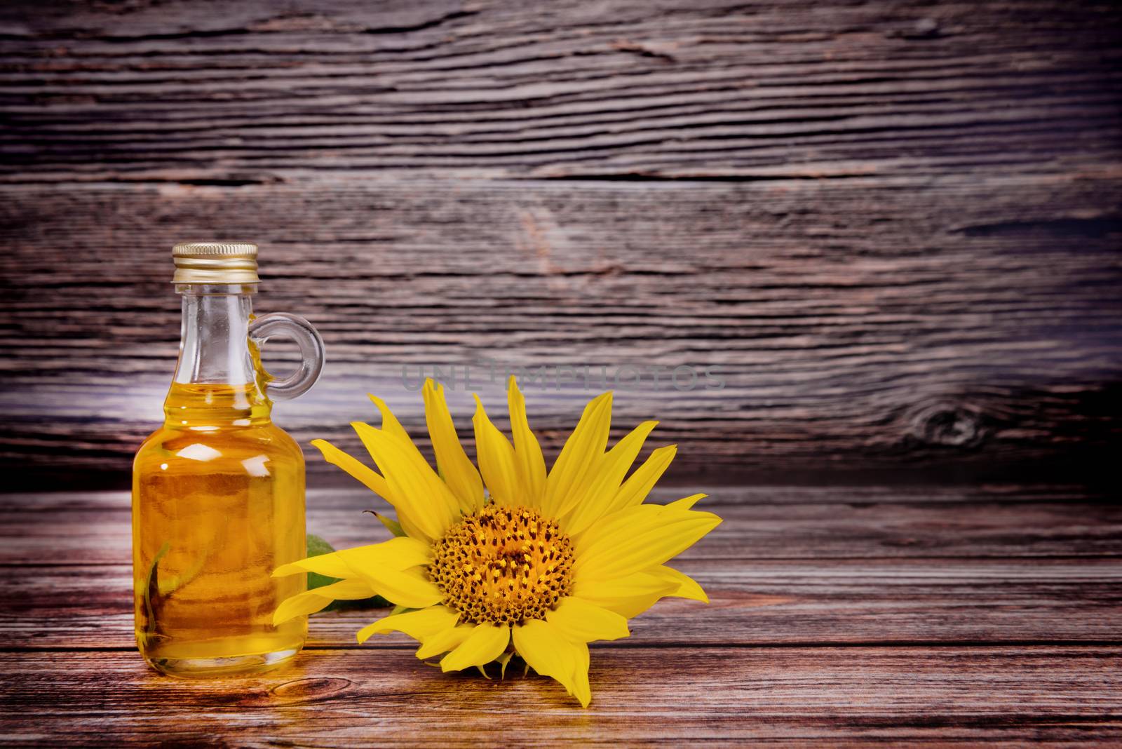 Glass bottle with sunflower oil and flowers on wooden background. Studio shot. by leonik