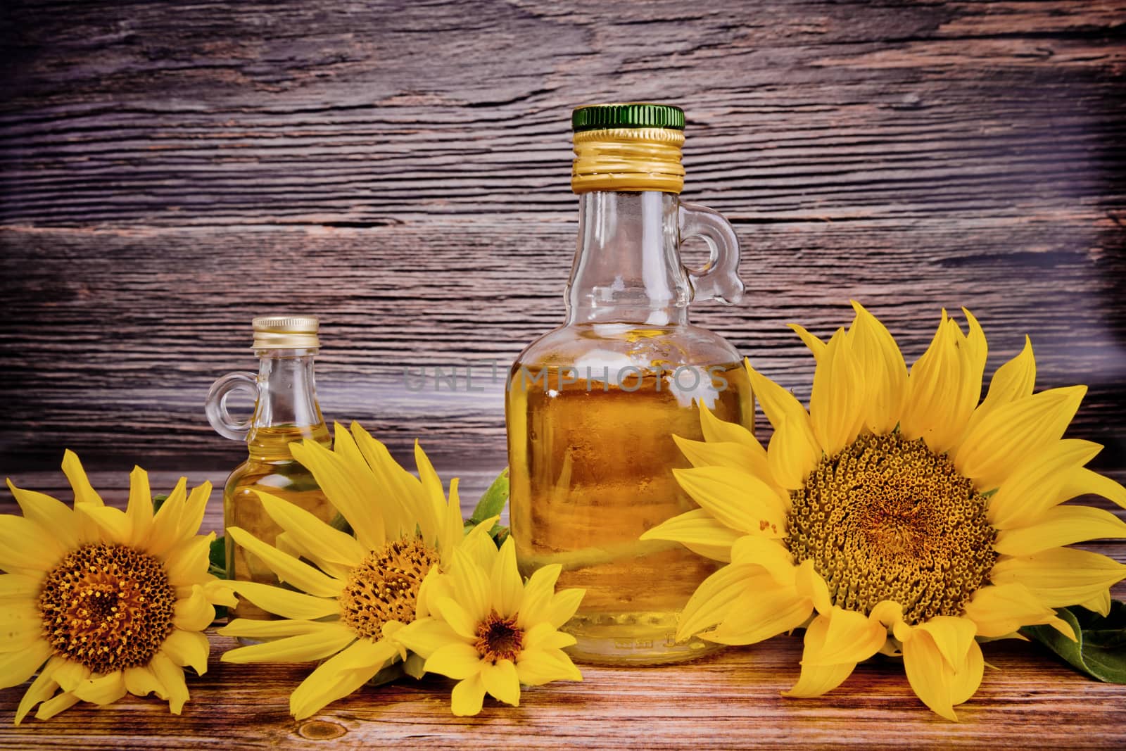 Two glass bottles with sunflower oil and flowers on wooden background. Studio shot.
