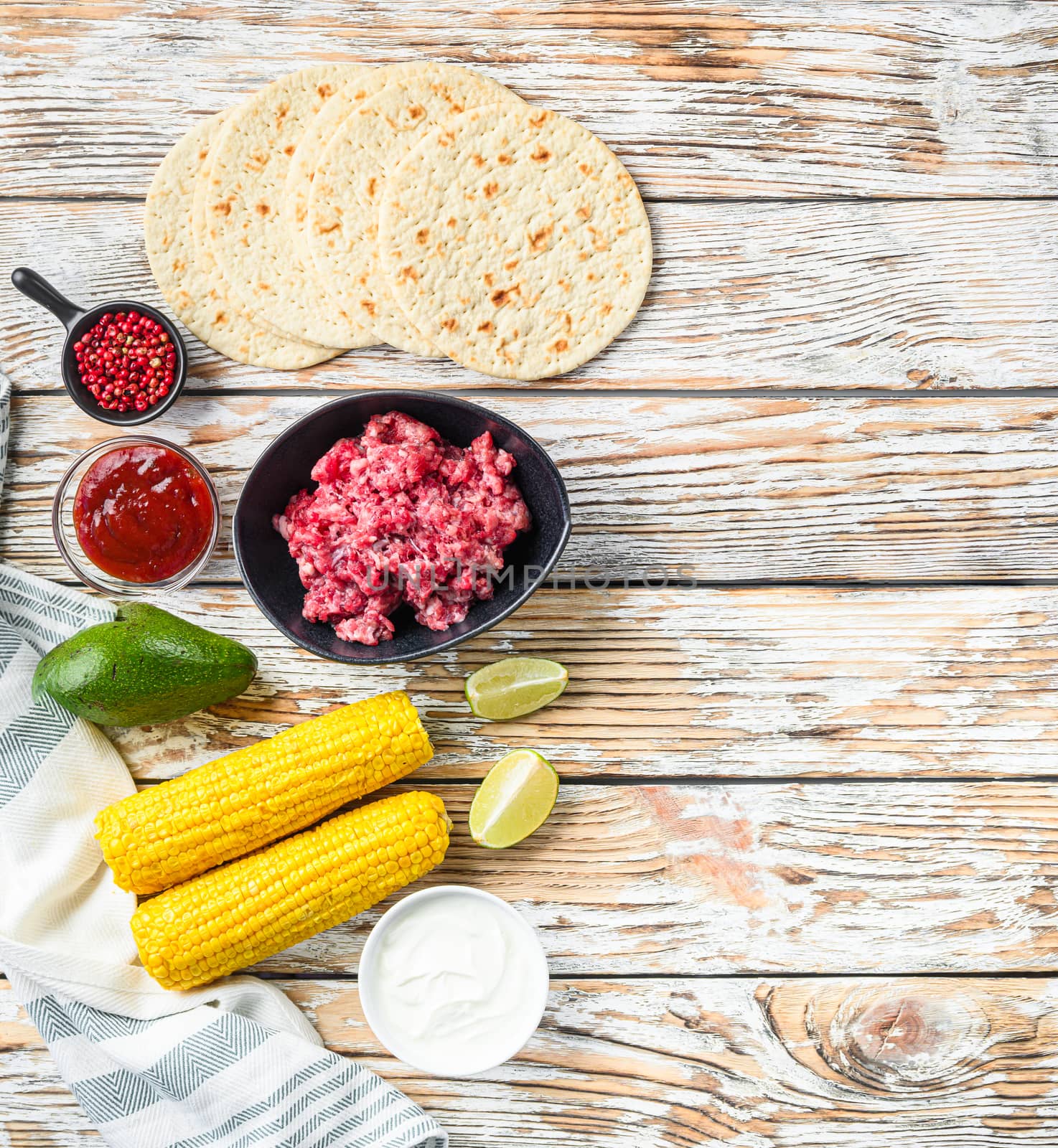 Cooking Mexican taco ingredients with minced organic beef meat in black bowl , corn, calsa over white textured wooden table, top view with space for text. by Ilianesolenyi