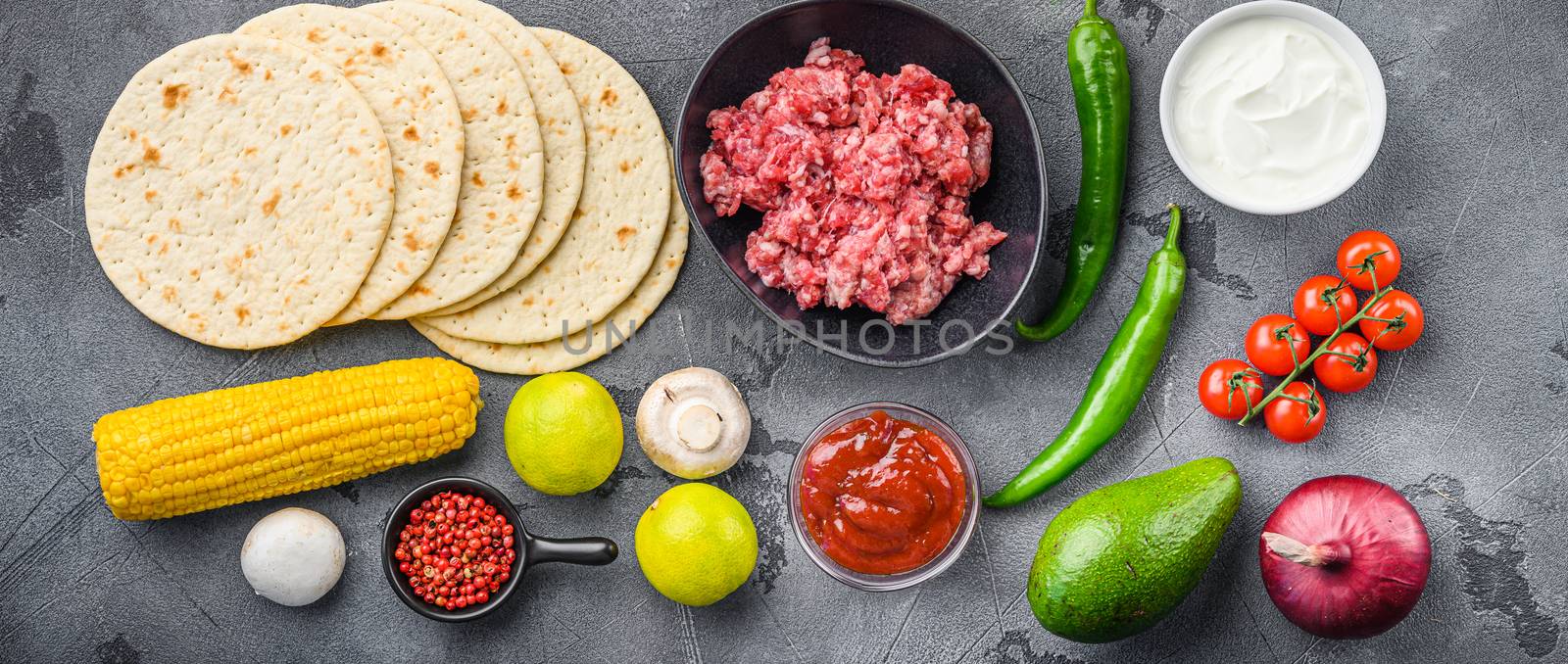 Traditional homemade taco ingredients with meat,salsa, peppers, tomatoes, avocado , corn, tortilla over grey background, top view