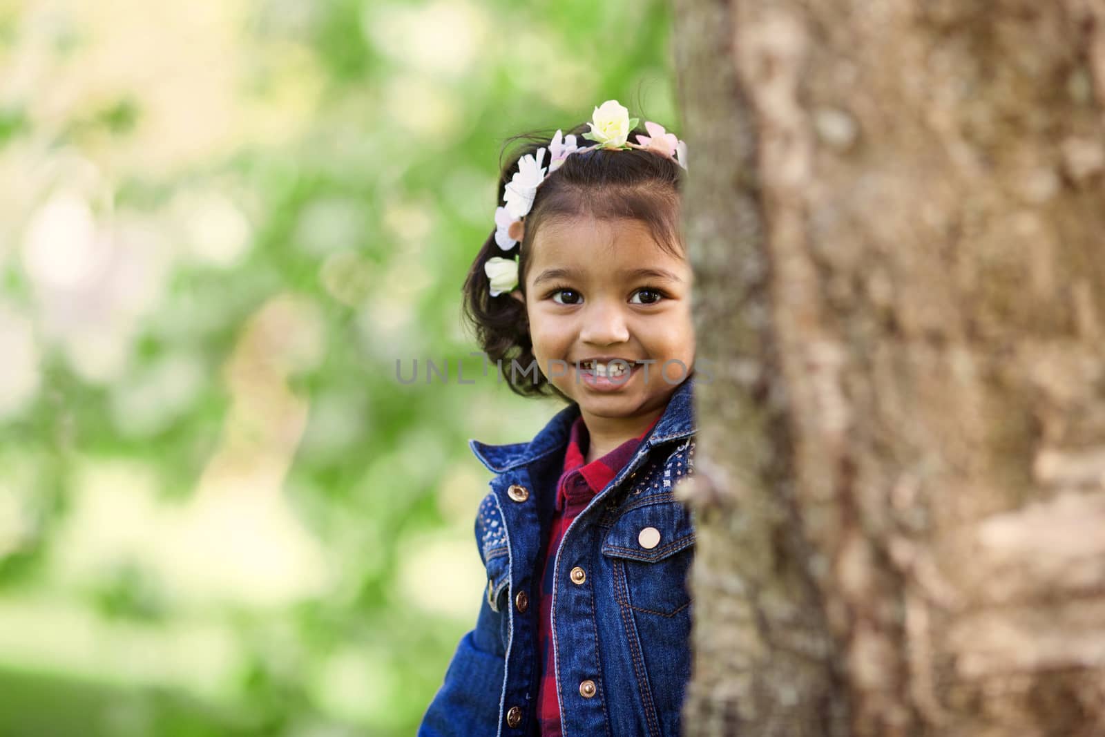 A small young girl at trunk of big tree in park by anry