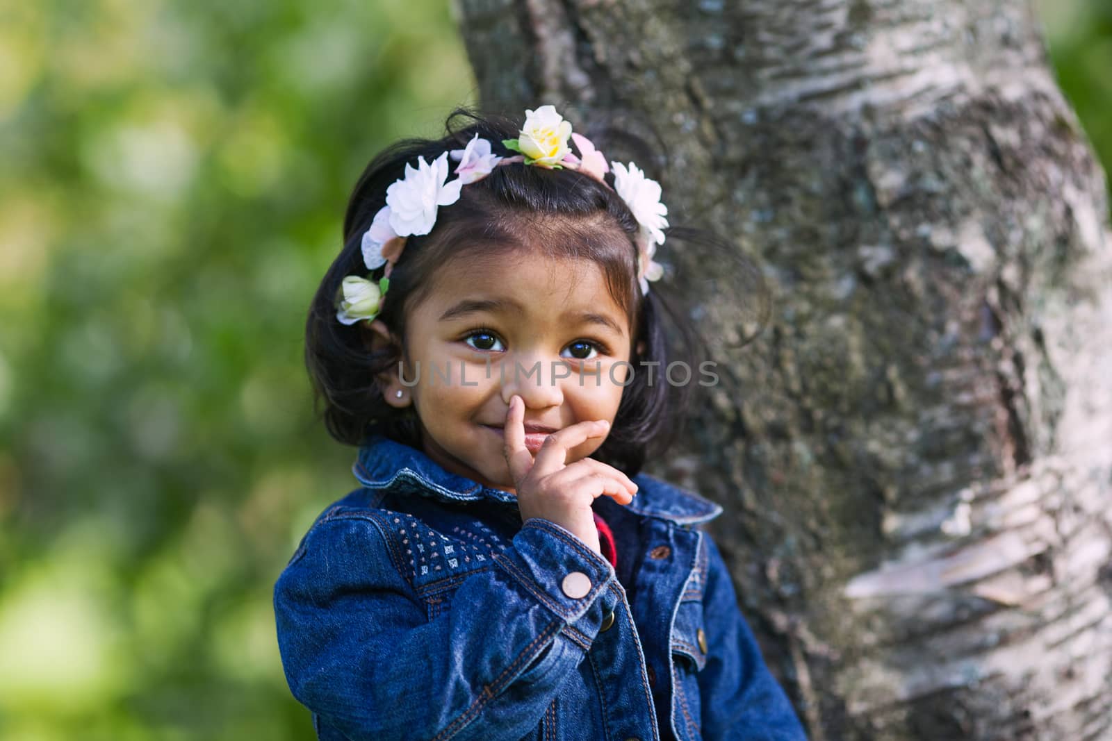 A two years old girl in park at a blooming branch of bird cherry tree by anry