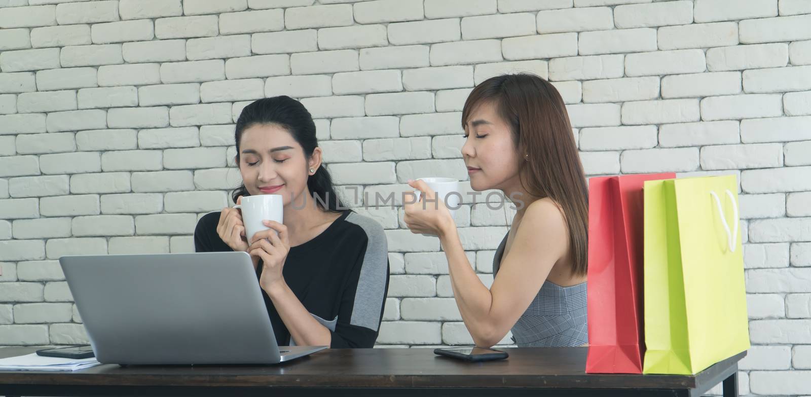 Two interesting Asian women were friends talking about coffee in a coffee shop. Two women sipping coffee And use computer laptops together