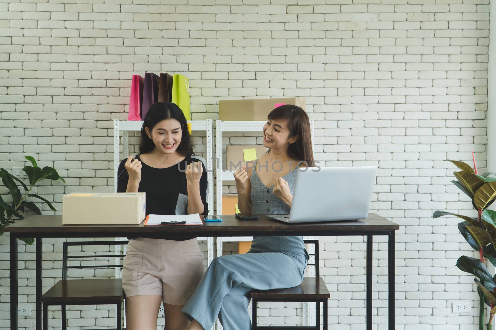 Two Asian female entrepreneurs, an online sales business owner, are chatting and checking orders from customers at home. The beautiful and attractive merchant is smiling happily for the startup.