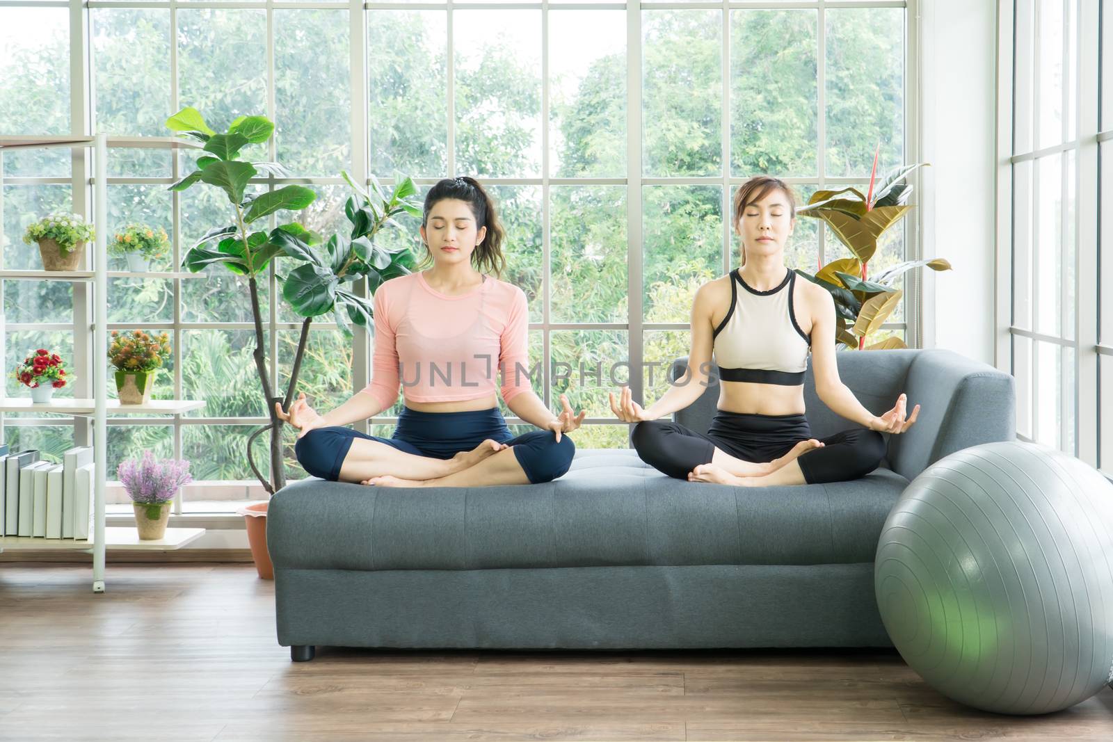 Attractive and healthy women Two Asians Exercising Stretching the muscles with yoga postures together at home. Help balance life
