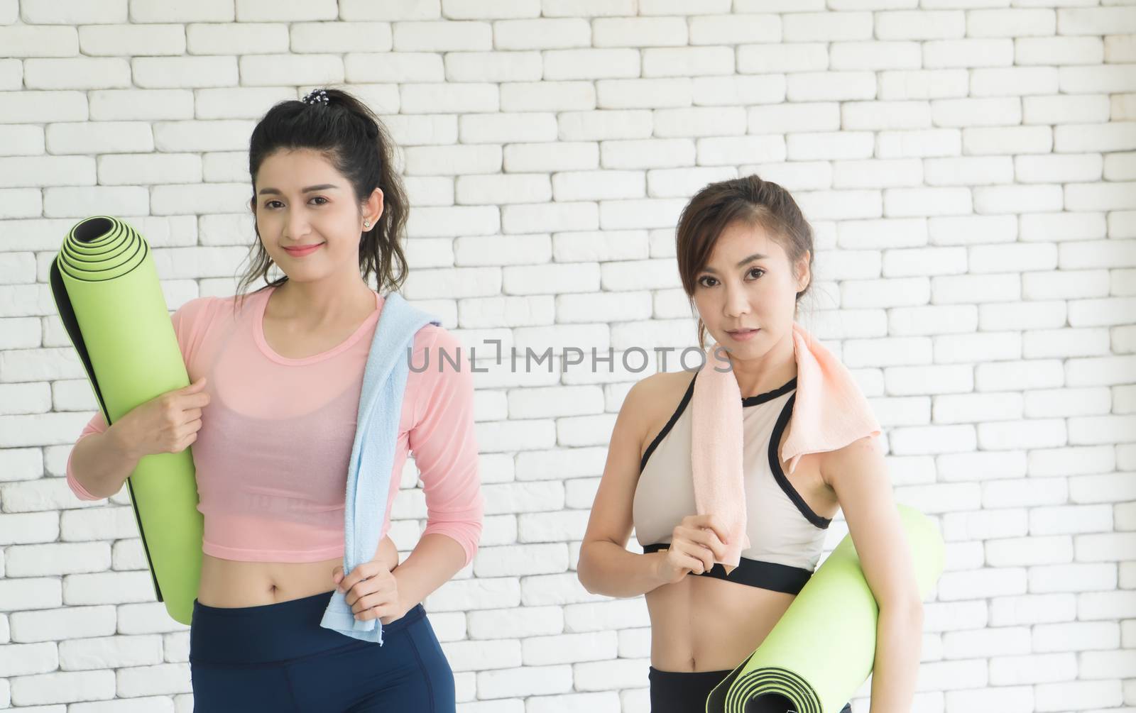 Portrait of a beautiful, attractive, healthy woman, two Asian people With exercise mats Talking in the gym After yoga