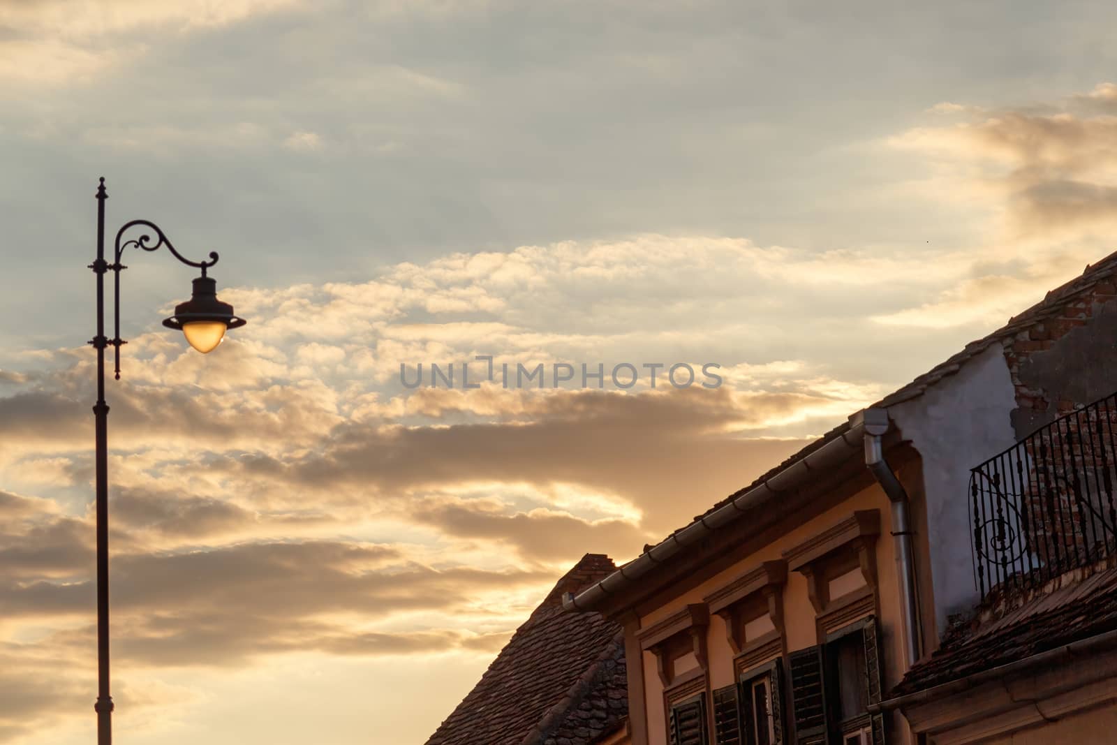 Concept of calm and serenity. Street lamp with colorful and cloudy sunset in the background. Sibiu, Romania, old medieval town in eastern central Europe. by dugulan