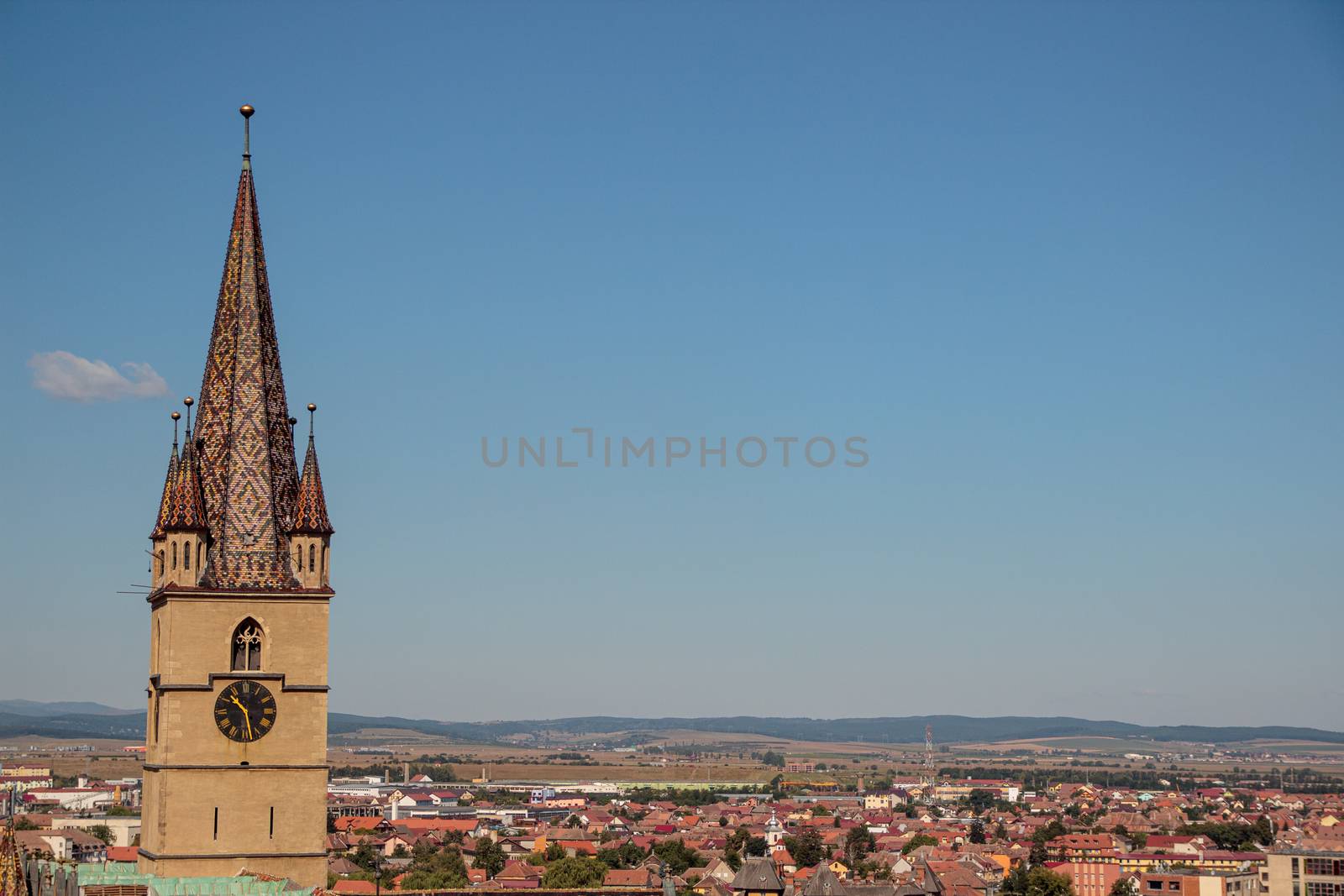 SIBIU, ROMANIA - Circa 2020: High view of old medieval town with cloudy blue sky. Beautiful tourist spot in eastern central Europe. Aerial view of famous Evangelic Church in Sibiu Romania by dugulan