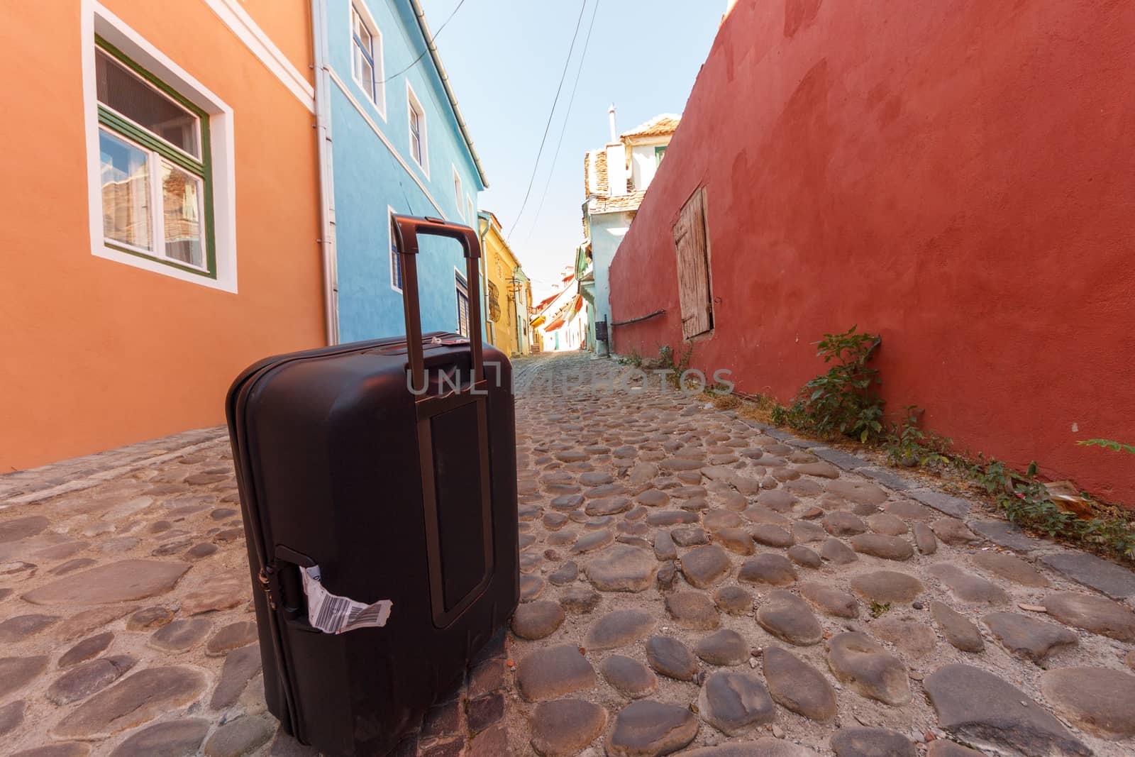 Black troler suitcase on an empty medieval city street. Colorful buildings and stone paved street with blue sky. Travel concept.