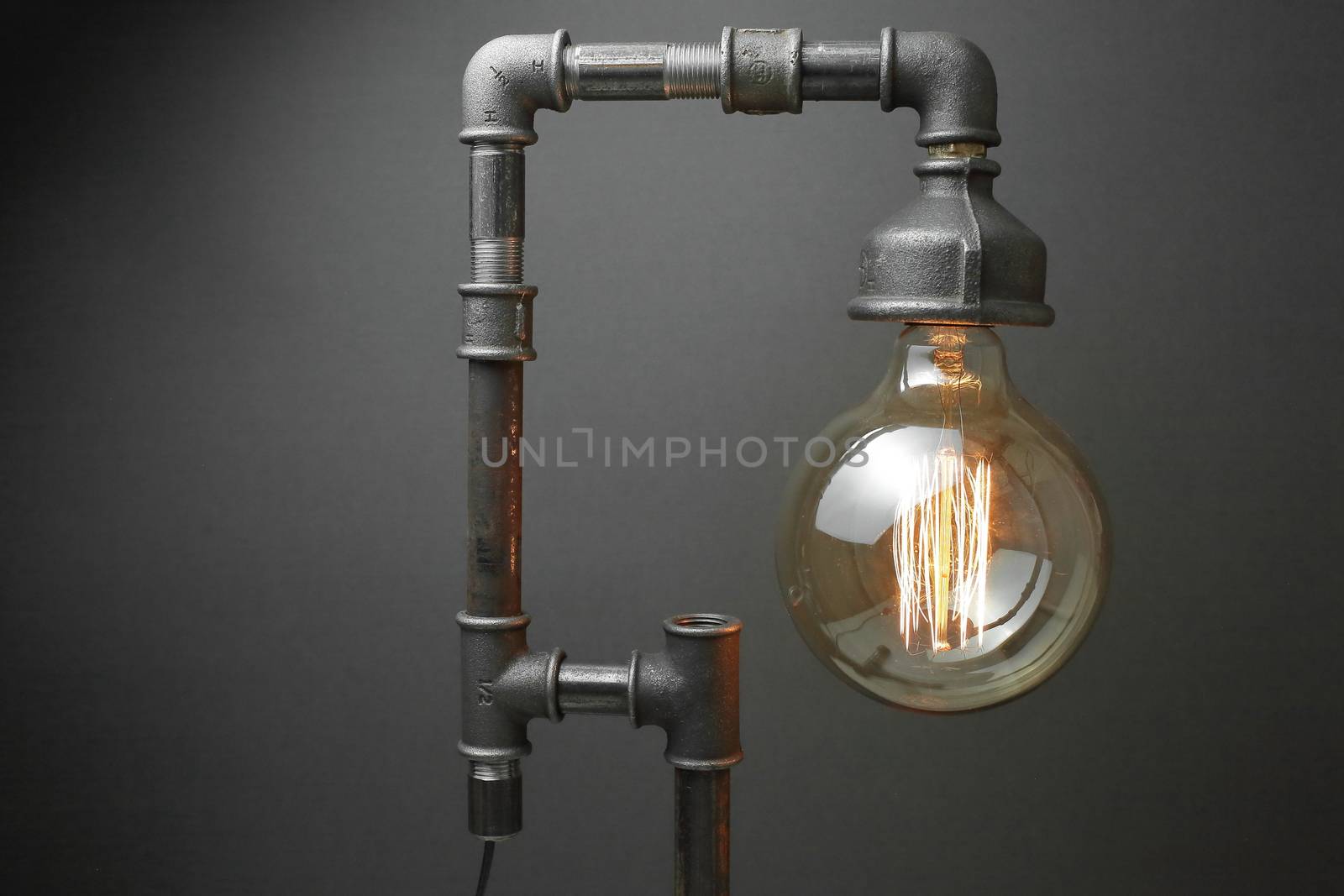 Retro lamp made of metal water pipes with an Edison lamp on a gray background. The concept is a good idea. High quality photo