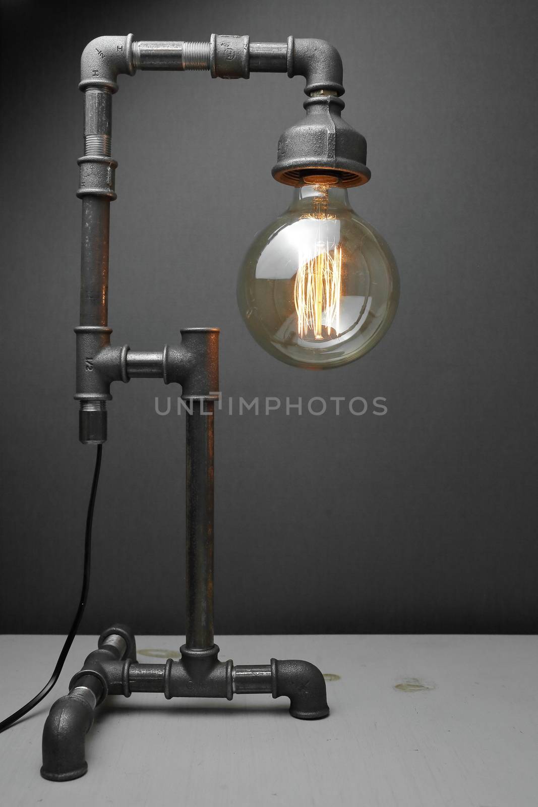 Retro lamp made of metal water pipes with an Edison lamp on a gray background. The concept is a good idea. by selinsmo
