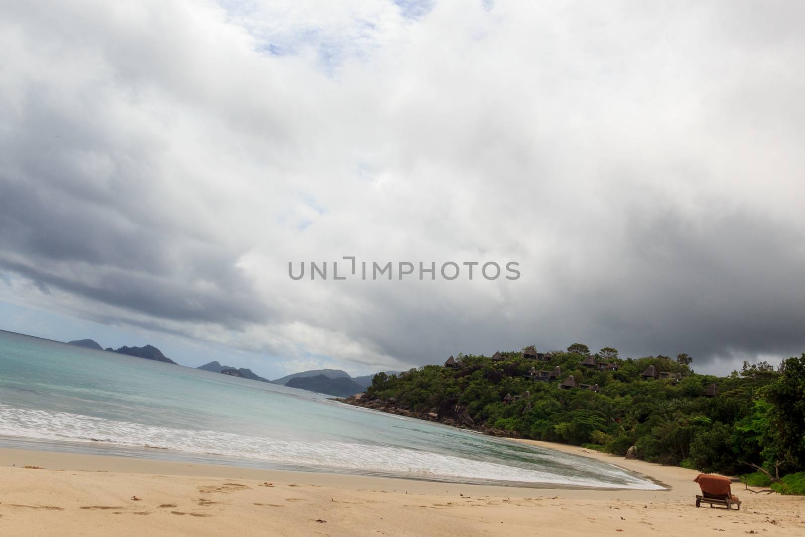 Beautiful view of Seychelles beach with a single chair in the sand on a cloudy warm day. Concept of tourist islands.