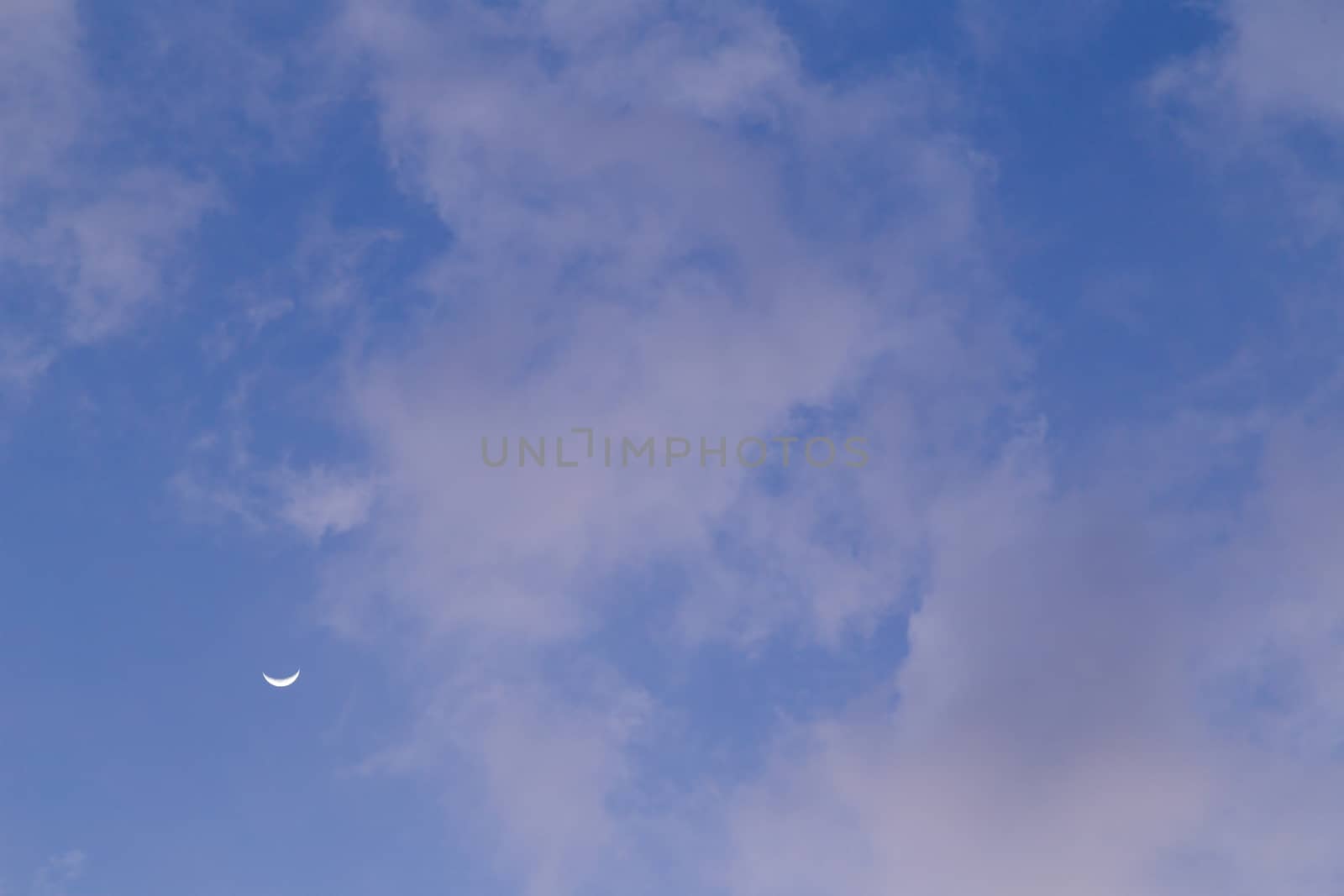 Moon behind the clouds during the day on a bright blue sky.