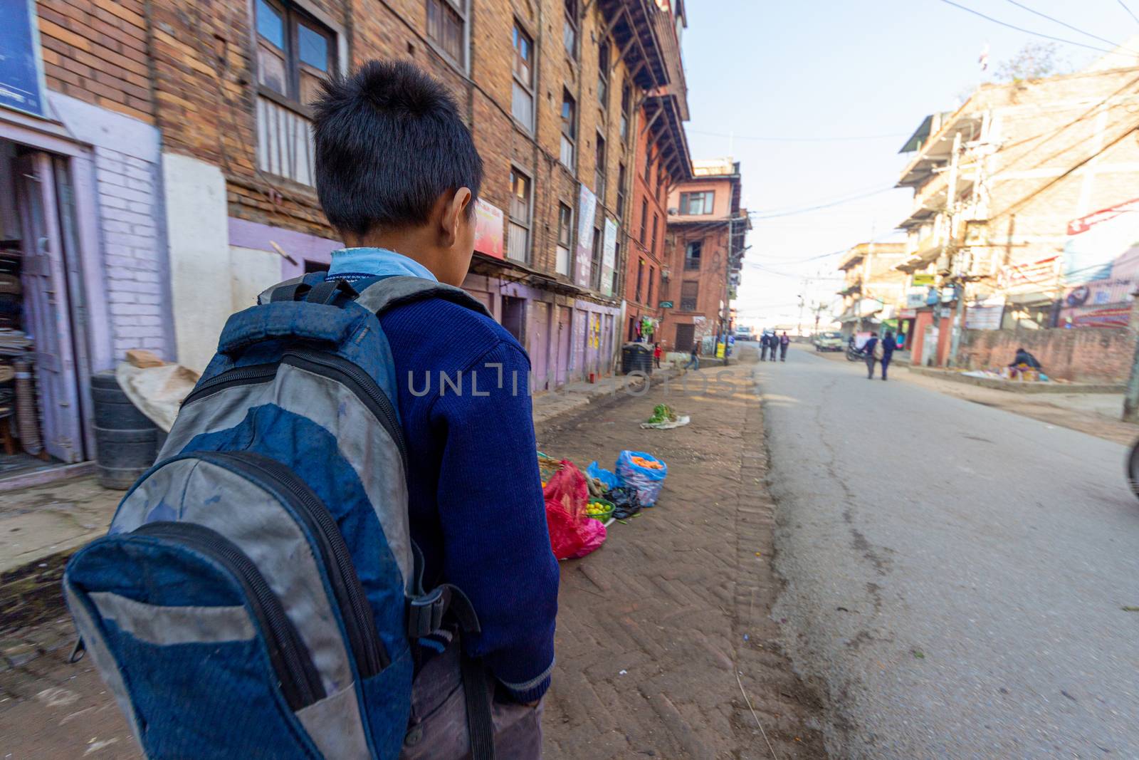 Kathmandu, Nepal - CIRCA 2020: Nepal, Kathmandu kid walking on an unpaved street to school with his back pack in the back. Concept of poverty schooling.